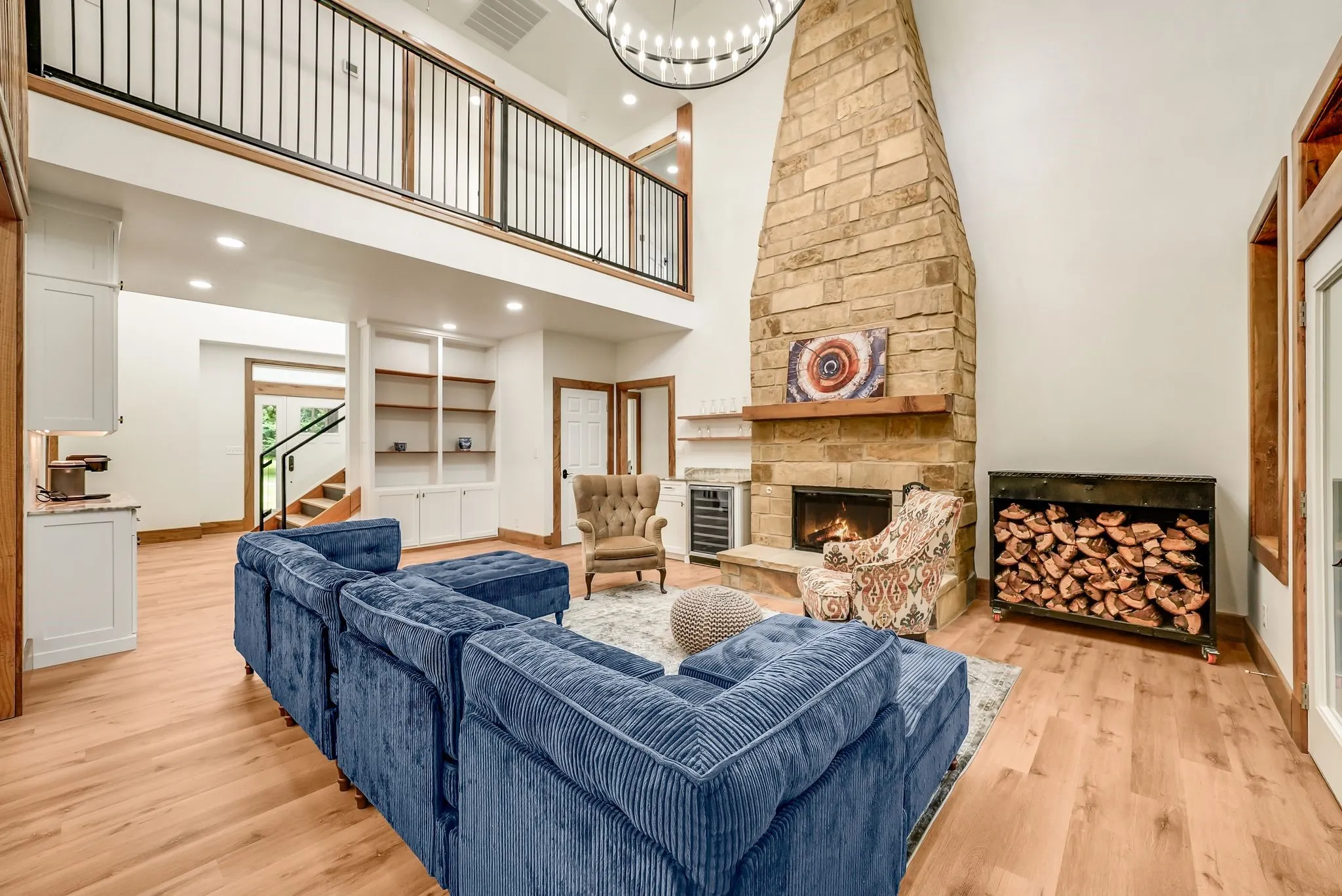 Two-story living area featuring a stone fireplace with a wood mantle, wood-finish flooring, a metal-railed second-story balcony, built-in shelving, and recessed lighting