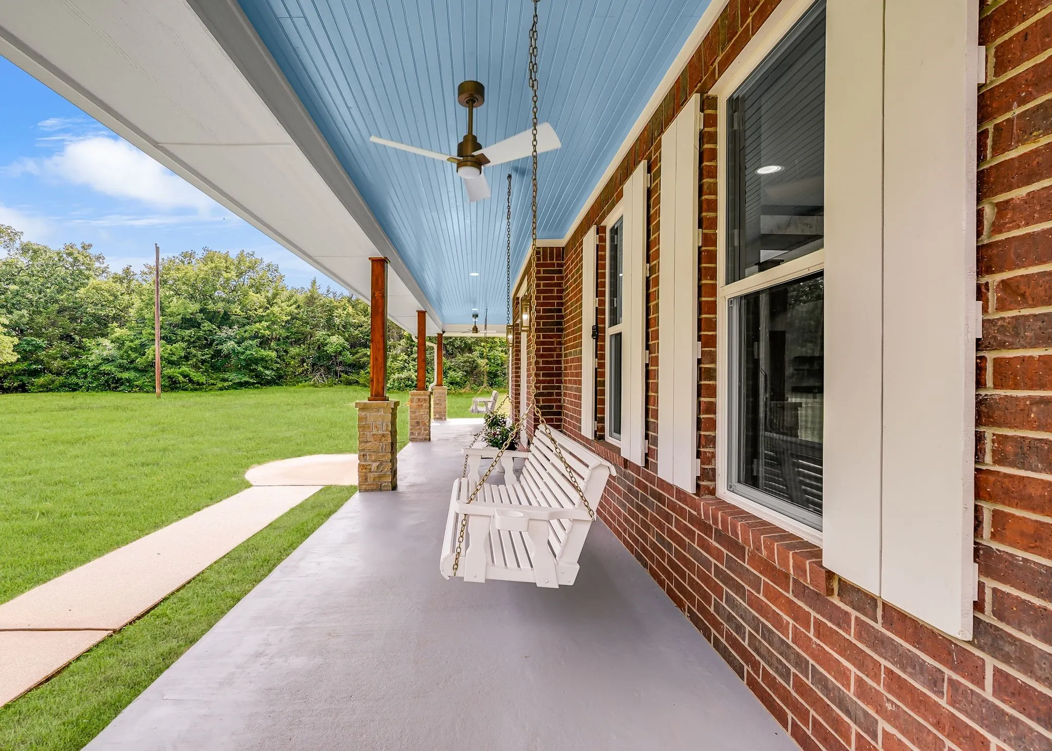 Expansive covered front porch featuring a light blue beadboard ceiling with recessed lighting and ceiling fans