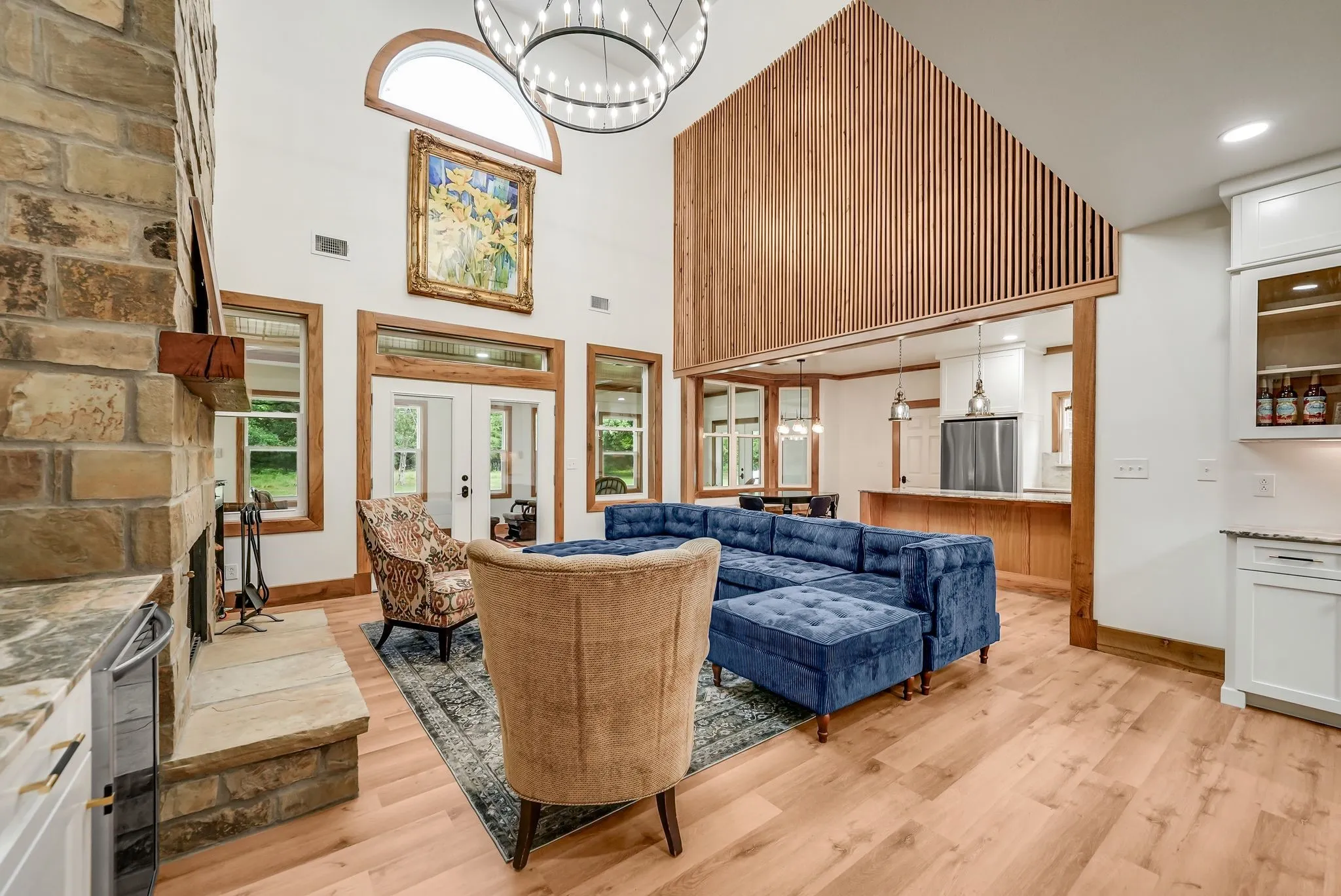 Vaulted living area featuring a stone fireplace, wood-finish flooring, and multiple windows