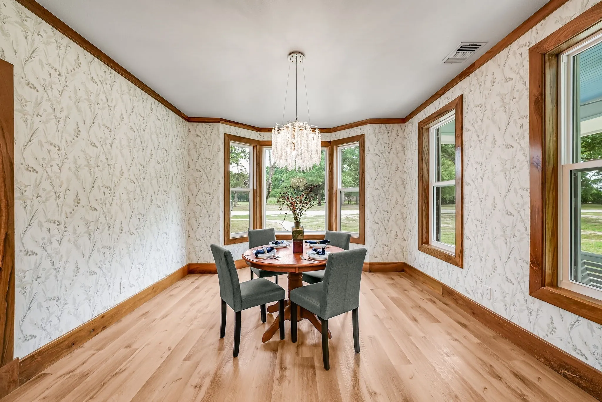 Dining space featuring wood-finish flooring, a contemporary chandelier, patterned wall treatment, and multiple windows with wood trim