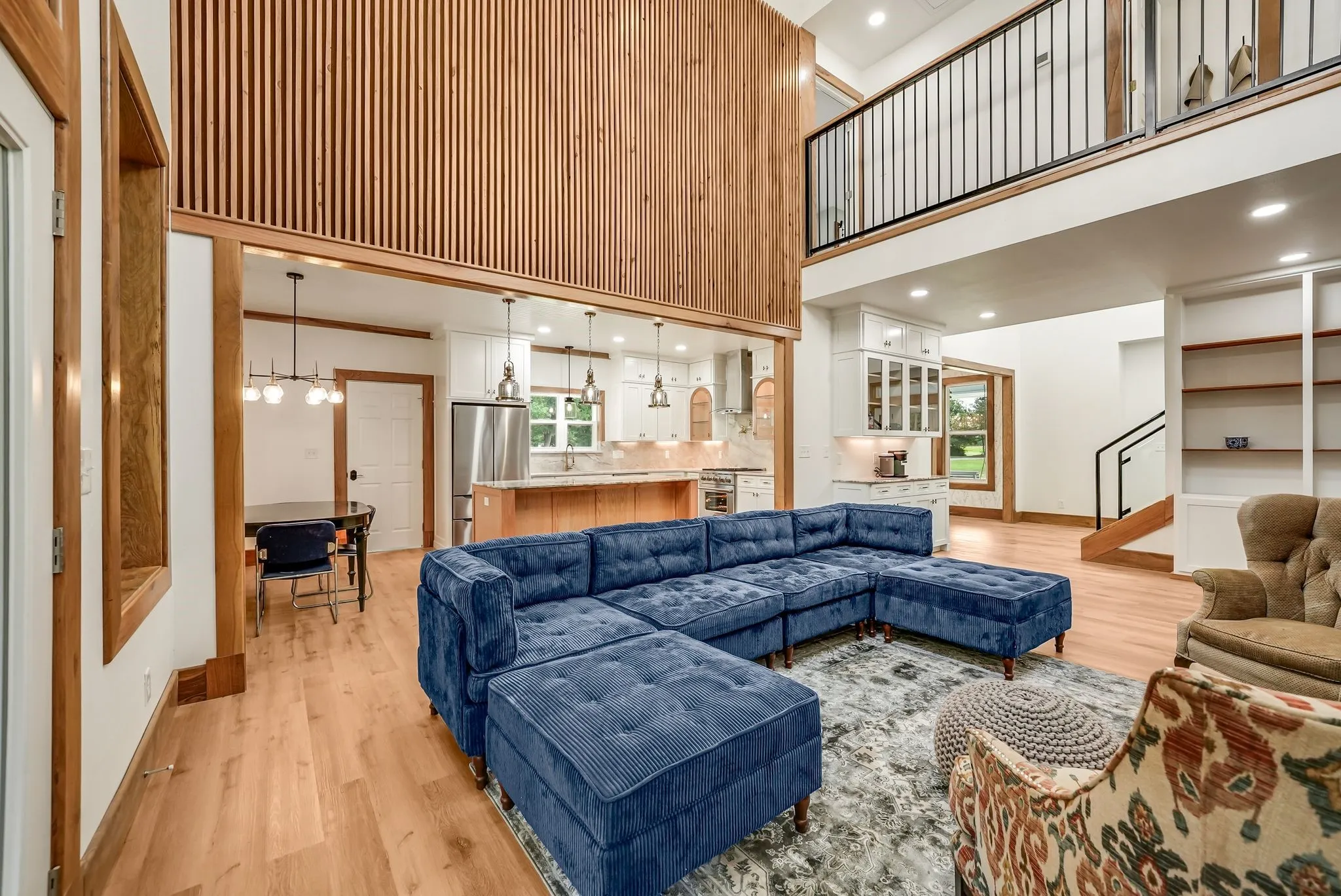 Vaulted ceilings with a wood slat accent wall, wood-finish flooring, and a second-story overlook featuring an open railing
