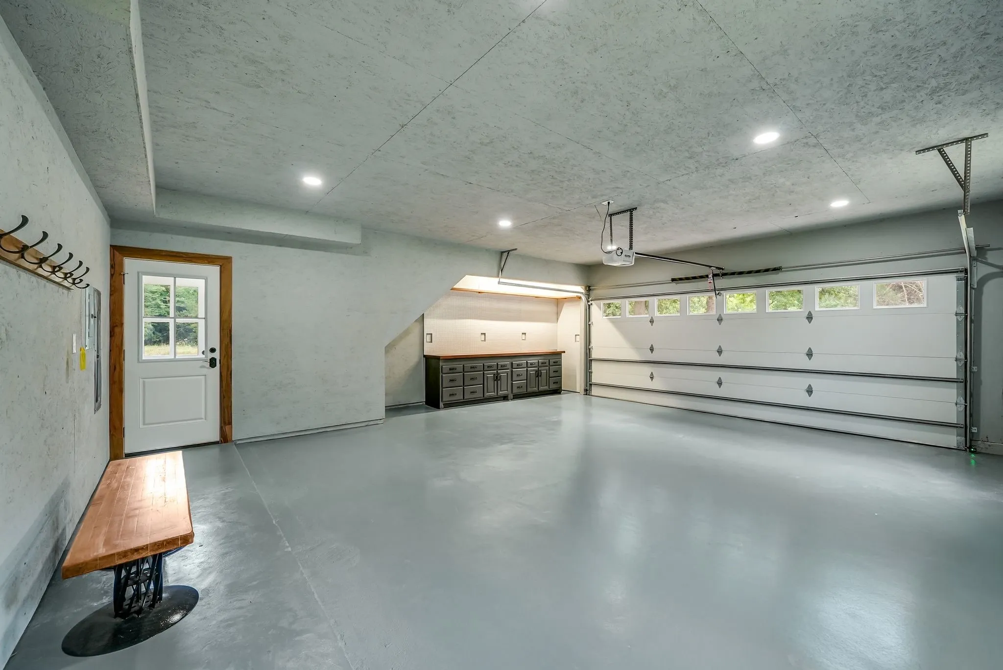 Spacious garage featuring a light gray epoxy floor, recessed lighting, built-in cabinetry with a wood-finish countertop, and a white garage door with upper window panels