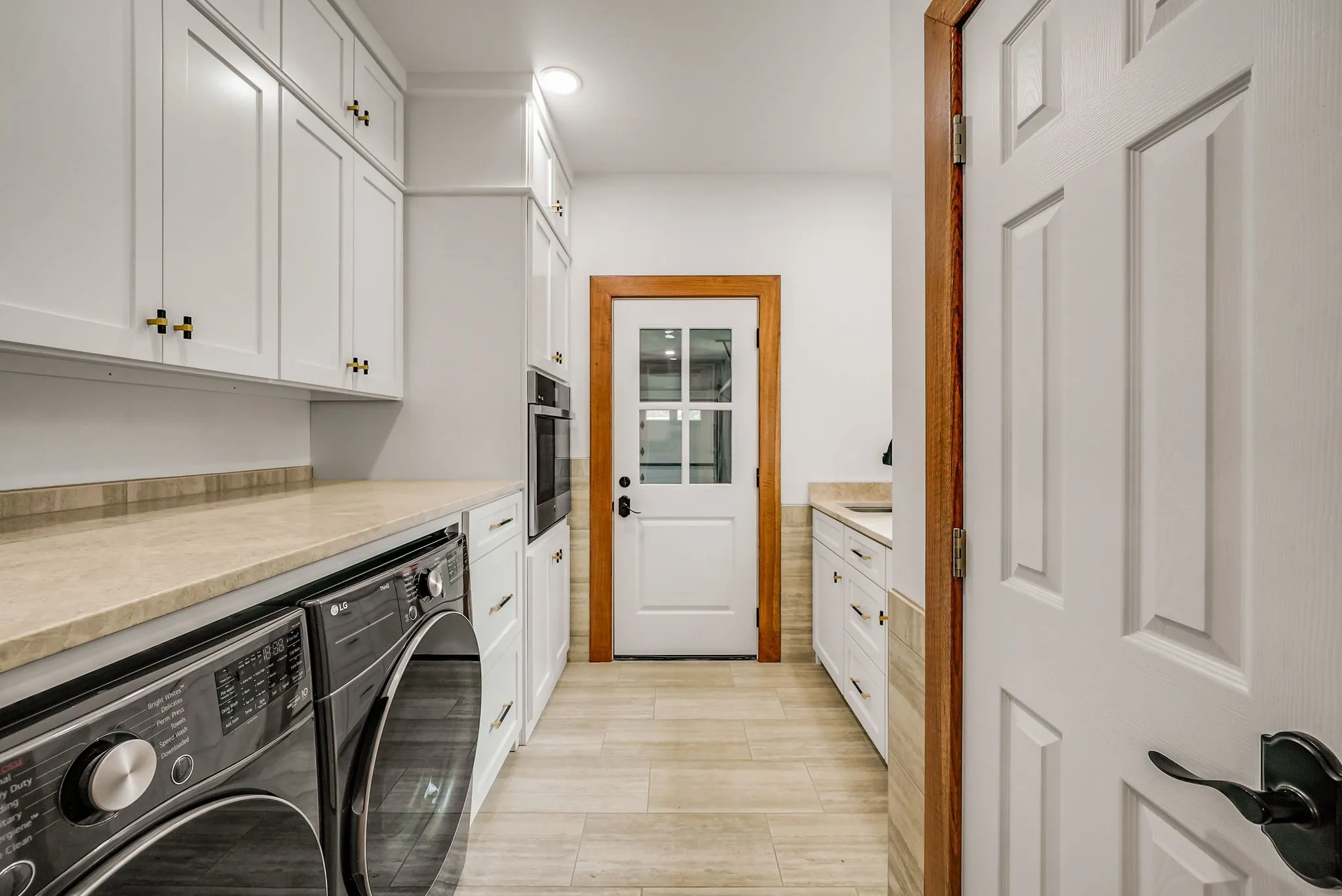 Utility space featuring white shaker-style cabinetry with gold-tone hardware, light-toned countertops, and light wood-finish flooring