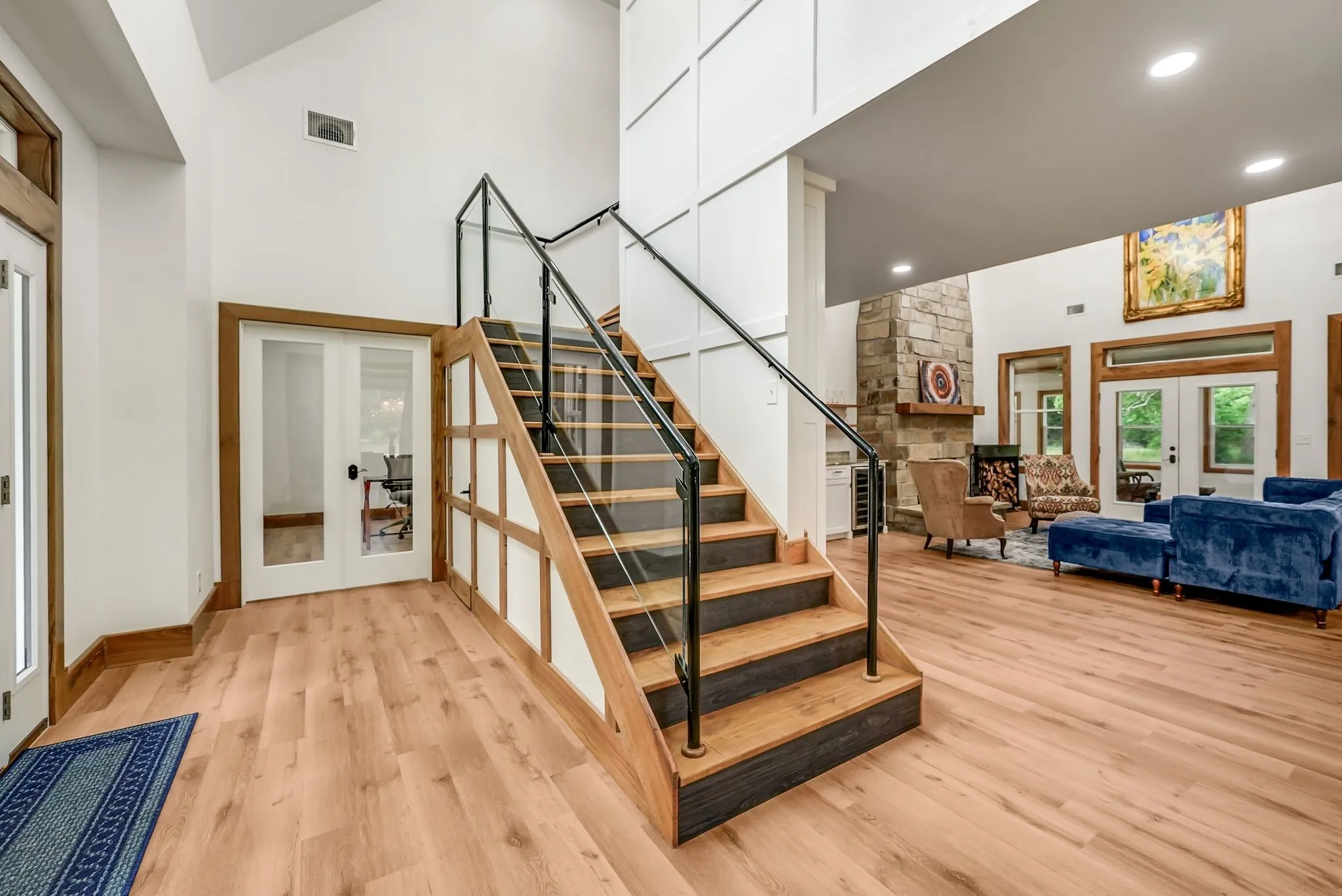 Grand entryway featuring a wood staircase with glass and black metal railings, leading to a spacious living area with wood-finish flooring