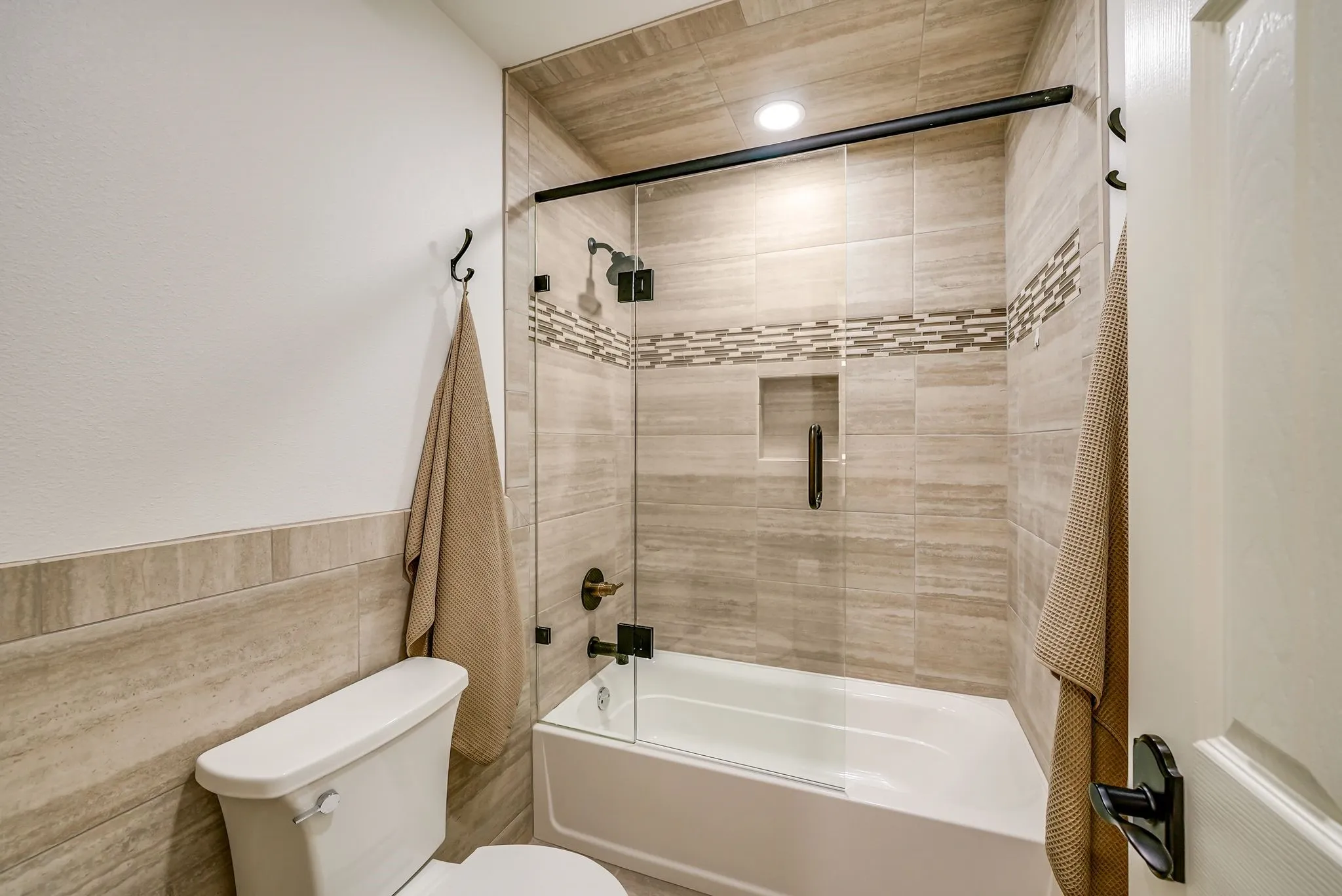 Full bathroom #3 on second floor featuring a tiled tub/shower combination with a clear glass enclosure, integrated shower niche, and dark bronze fixtures