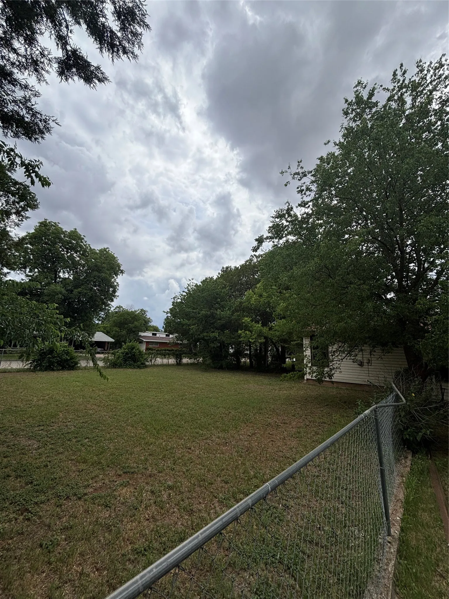 Expansive grassy yard with mature perimeter trees and a chain-link fence
