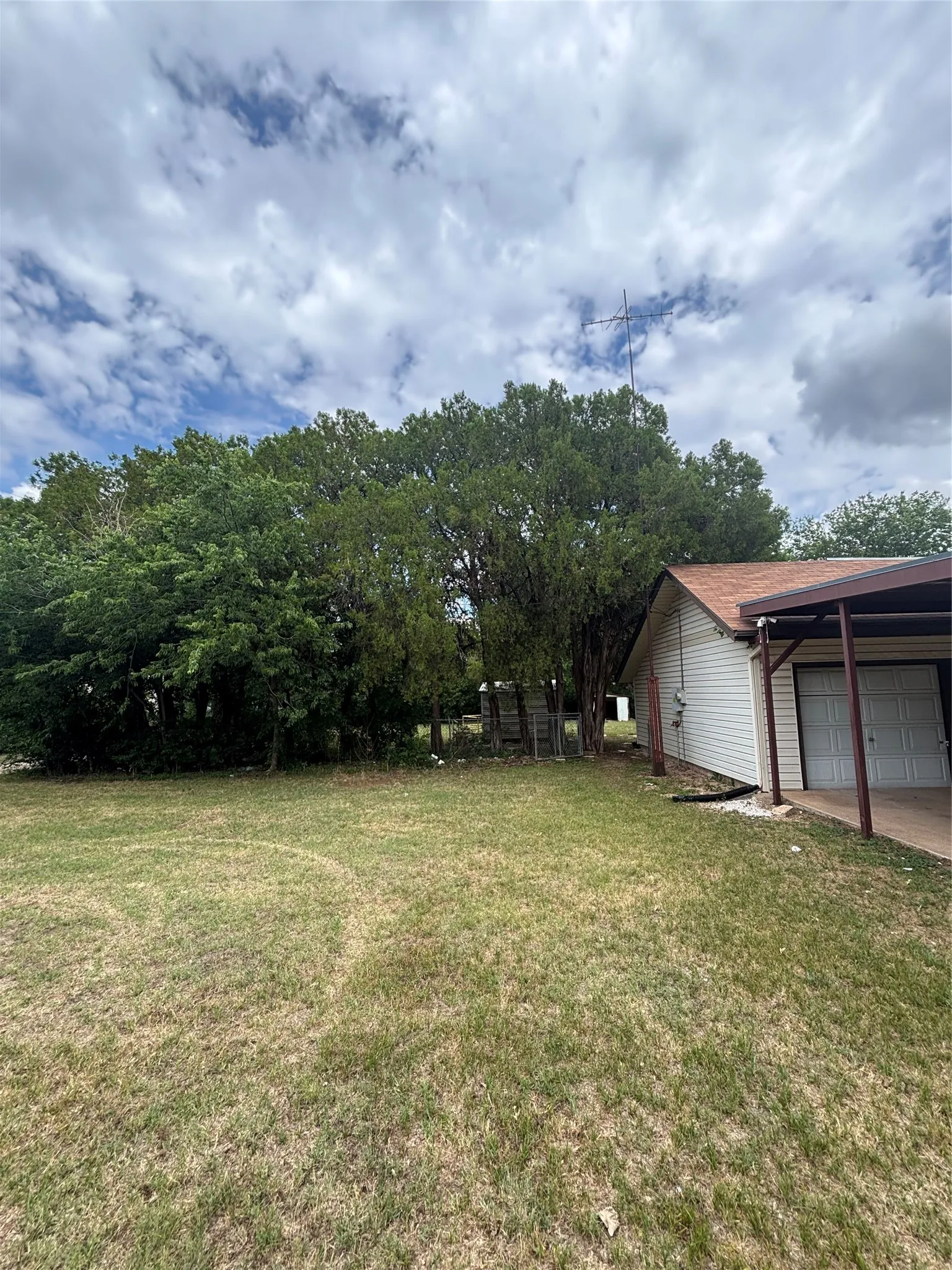 Spacious side yard featuring mature trees and a covered carport with two bays