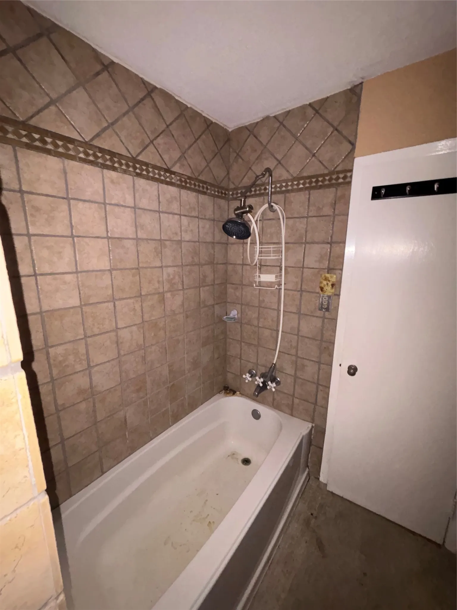Bathtub with a tiled surround featuring a decorative accent band and a dual-head shower fixture