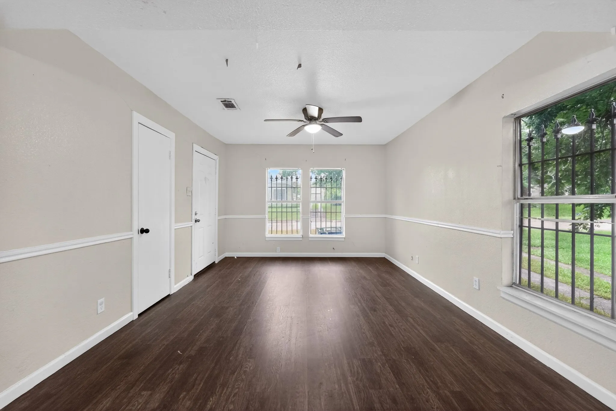 Spacious room featuring wood-finish flooring, light-toned walls with chair rail molding, and a ceiling fan with integrated lighting