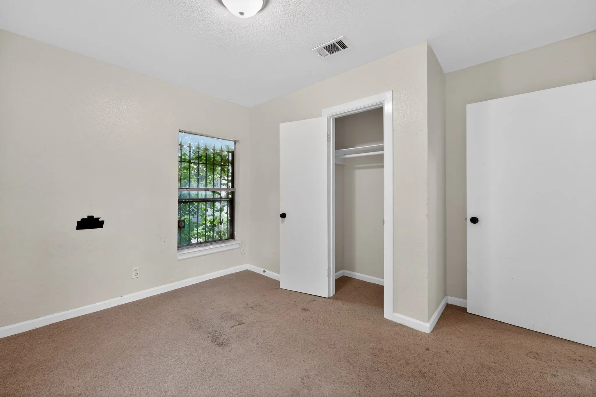 Room featuring a window with security bars, a built-in closet with double doors, and a ceiling-mounted light fixture