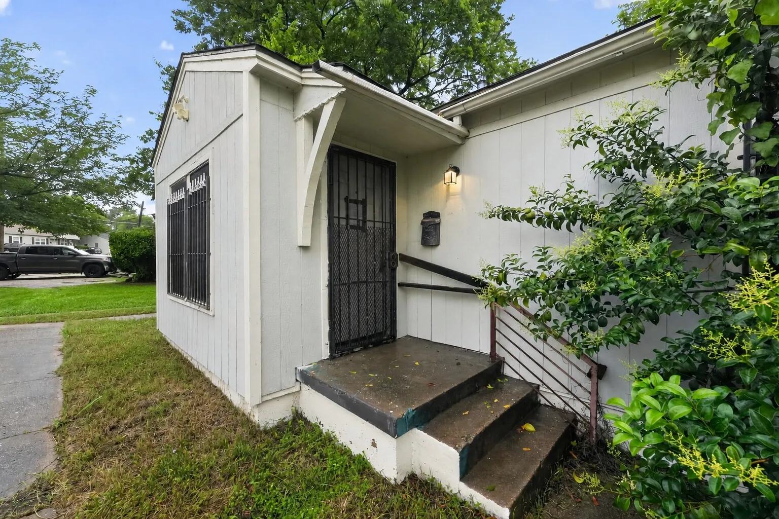 White vertical siding exterior with prominent front entry featuring a security door, overhead lighting, and a mailbox