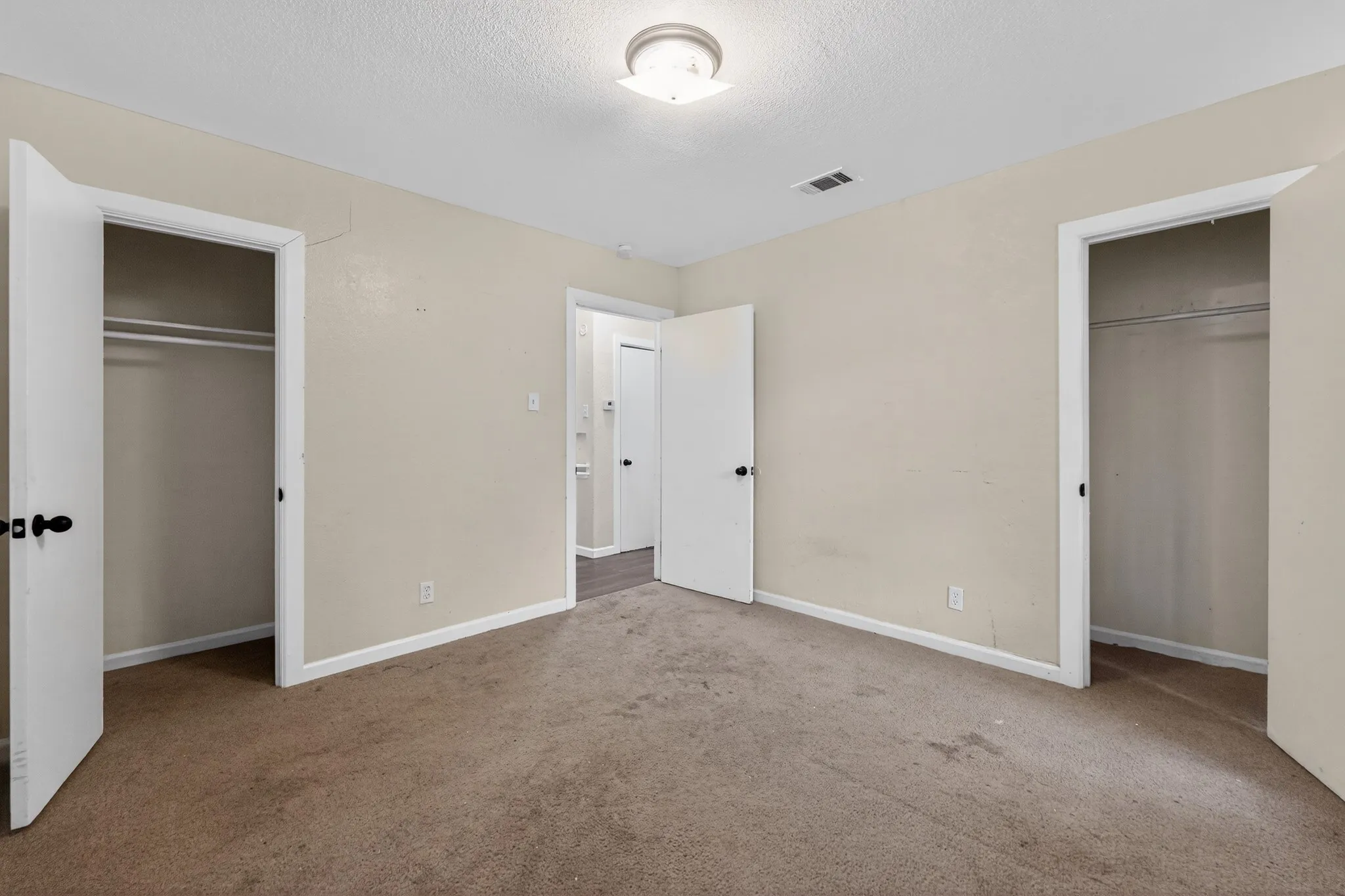 Neutral-toned walls and brown carpet flooring frame a room with two open closets