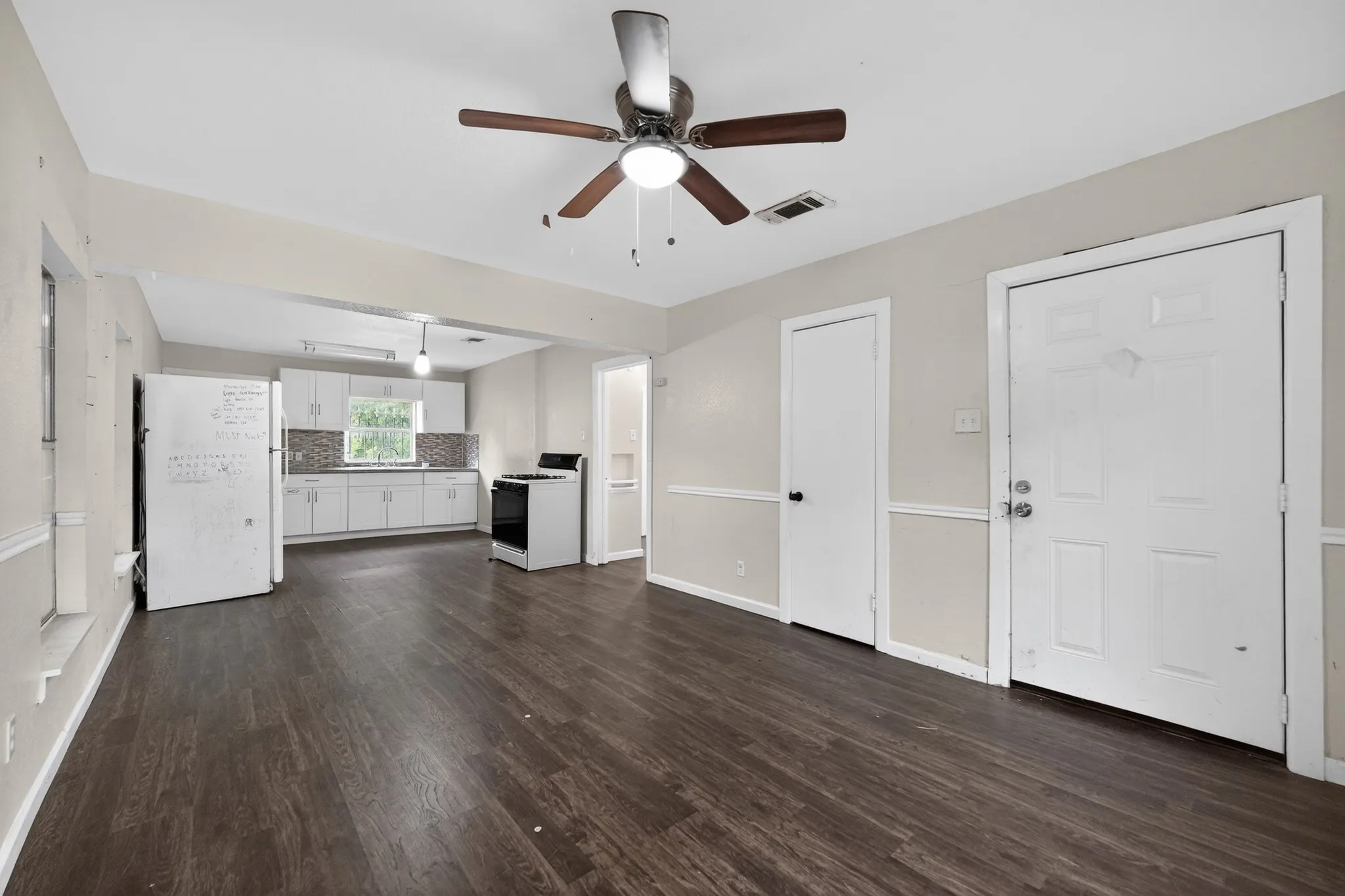 Open-concept living area featuring wood-finish flooring, a ceiling fan with integrated lighting, and neutral wall tones