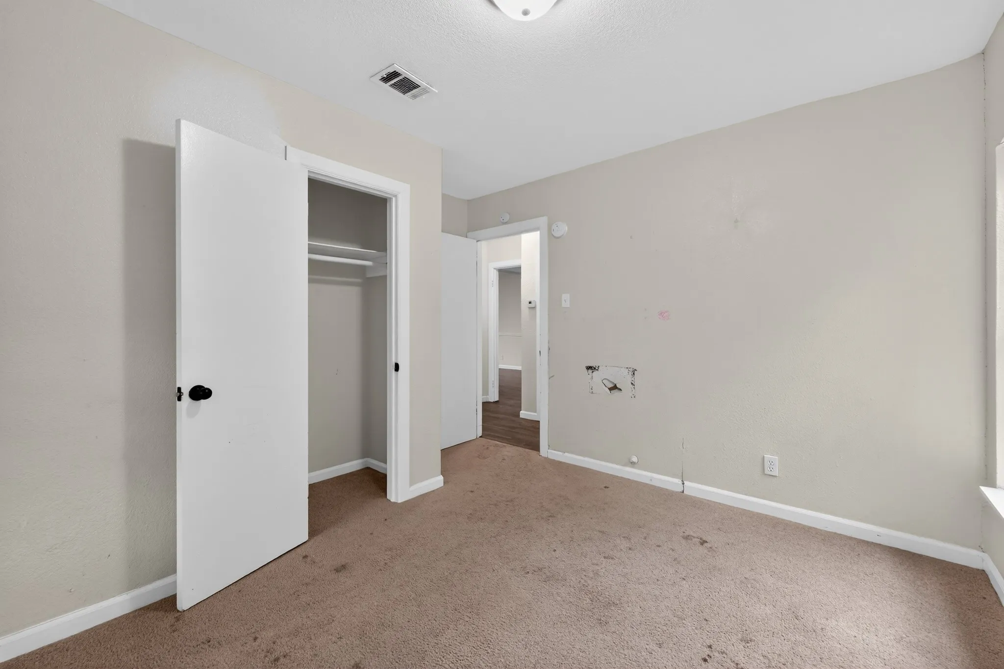 Neutral-toned room featuring a single window, a built-in closet with white doors, and a ceiling-mounted light fixture