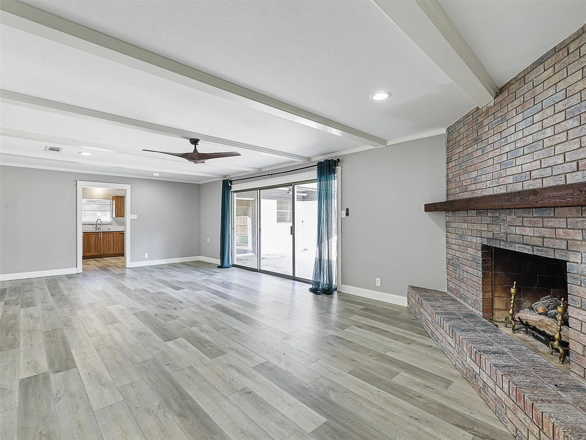 Spacious living room featuring exposed beam details, a statement brick fireplace, and seamless indoor-outdoor flow.