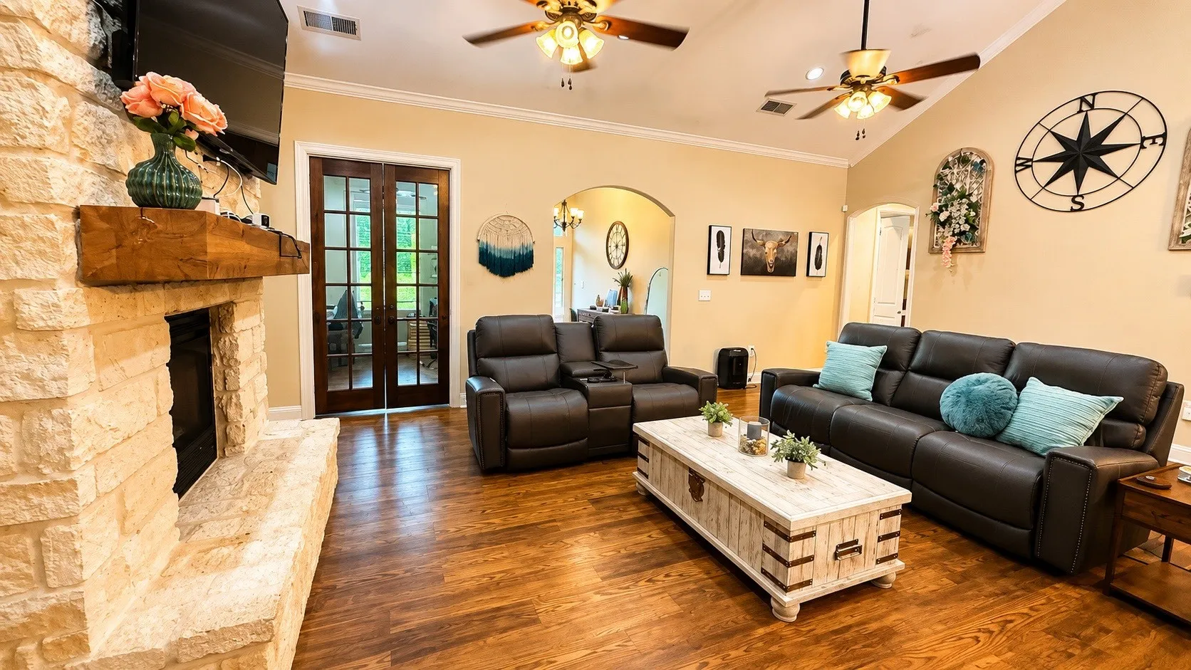 Spacious living area featuring a stacked stone fireplace with a substantial wood mantel, vaulted ceilings with ceiling fans, wood-finish flooring, and French doors