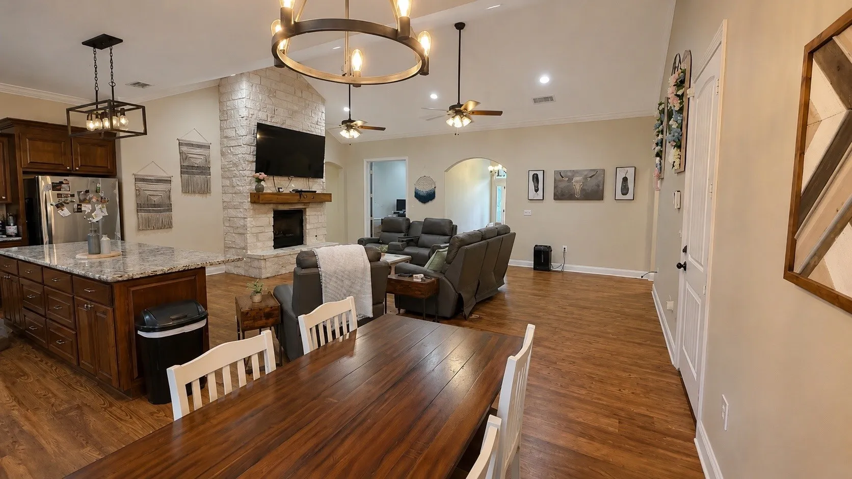 Open-concept living space featuring wood-finish flooring, a stone fireplace with a wood mantle, and a kitchen island with a light-colored countertop