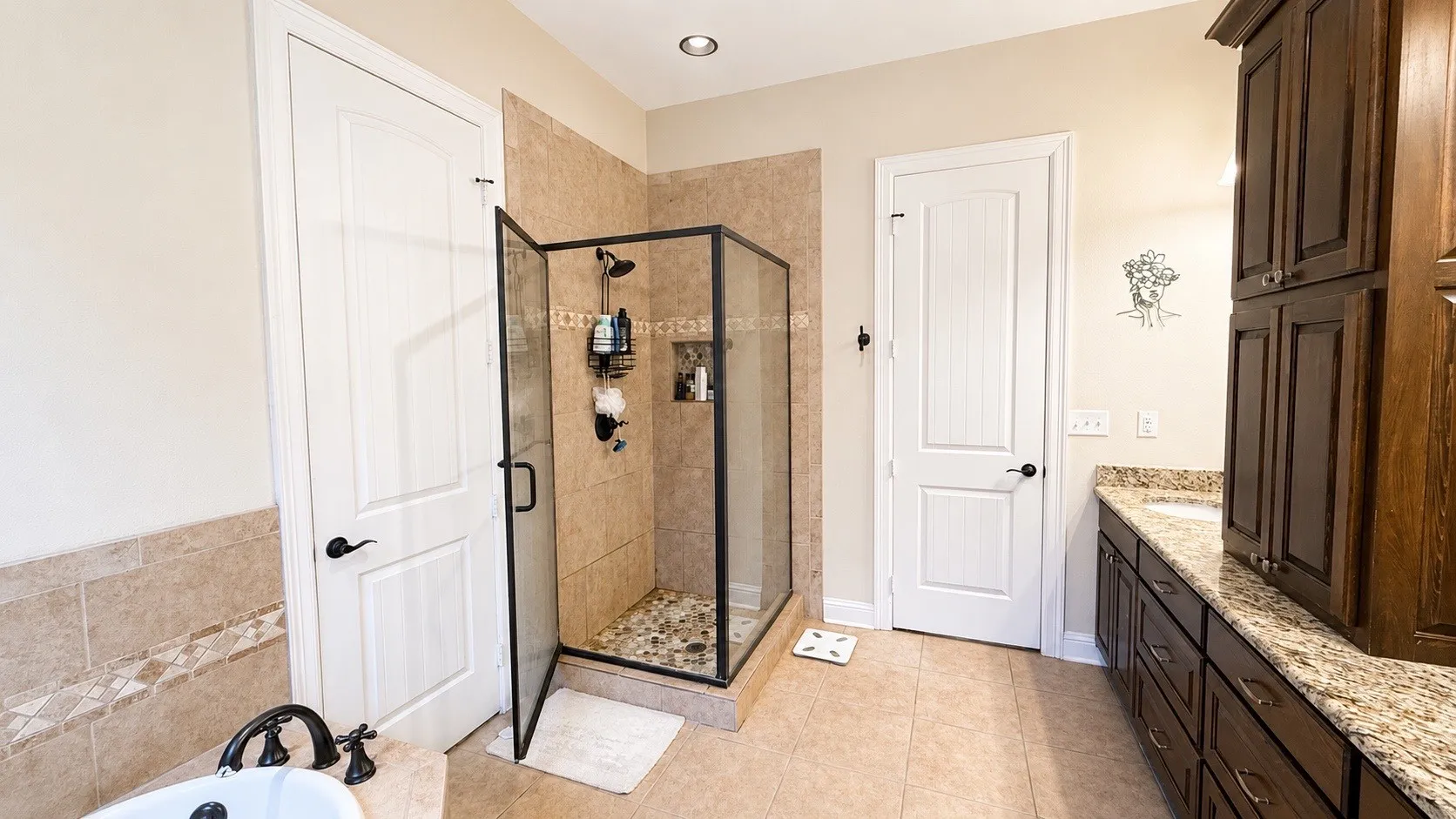 Glass-enclosed shower with pebble-finish floor and tiled walls