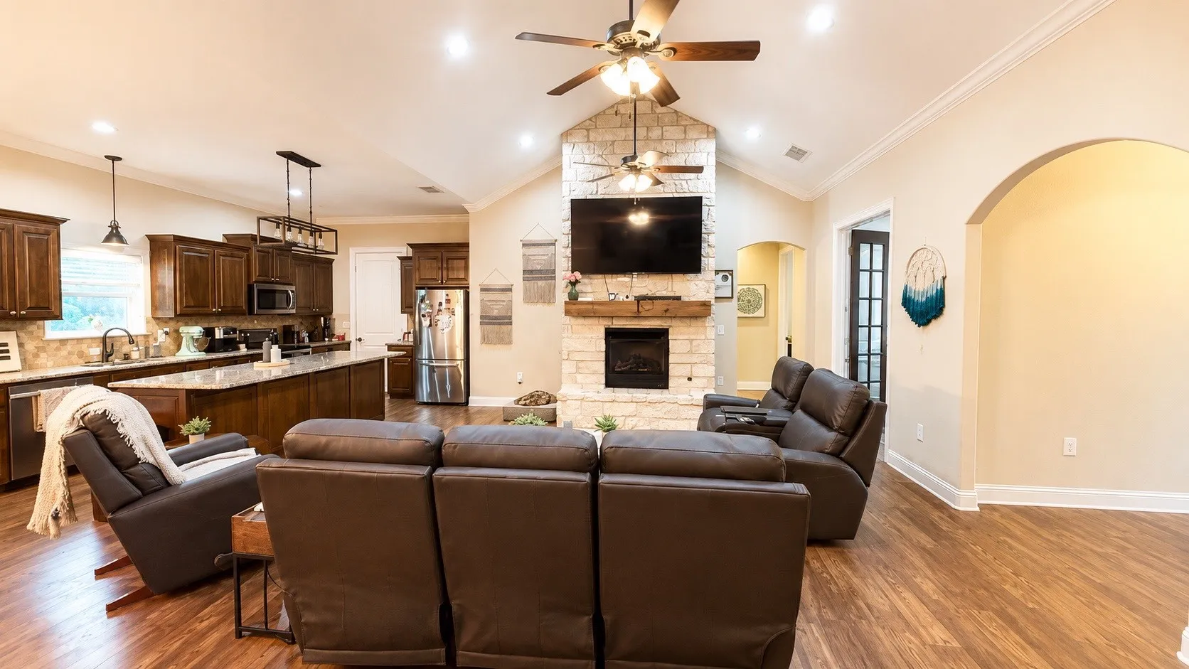 Spacious living area featuring a vaulted ceiling with a fan, a floor-to-ceiling stone fireplace, and wood-finish flooring