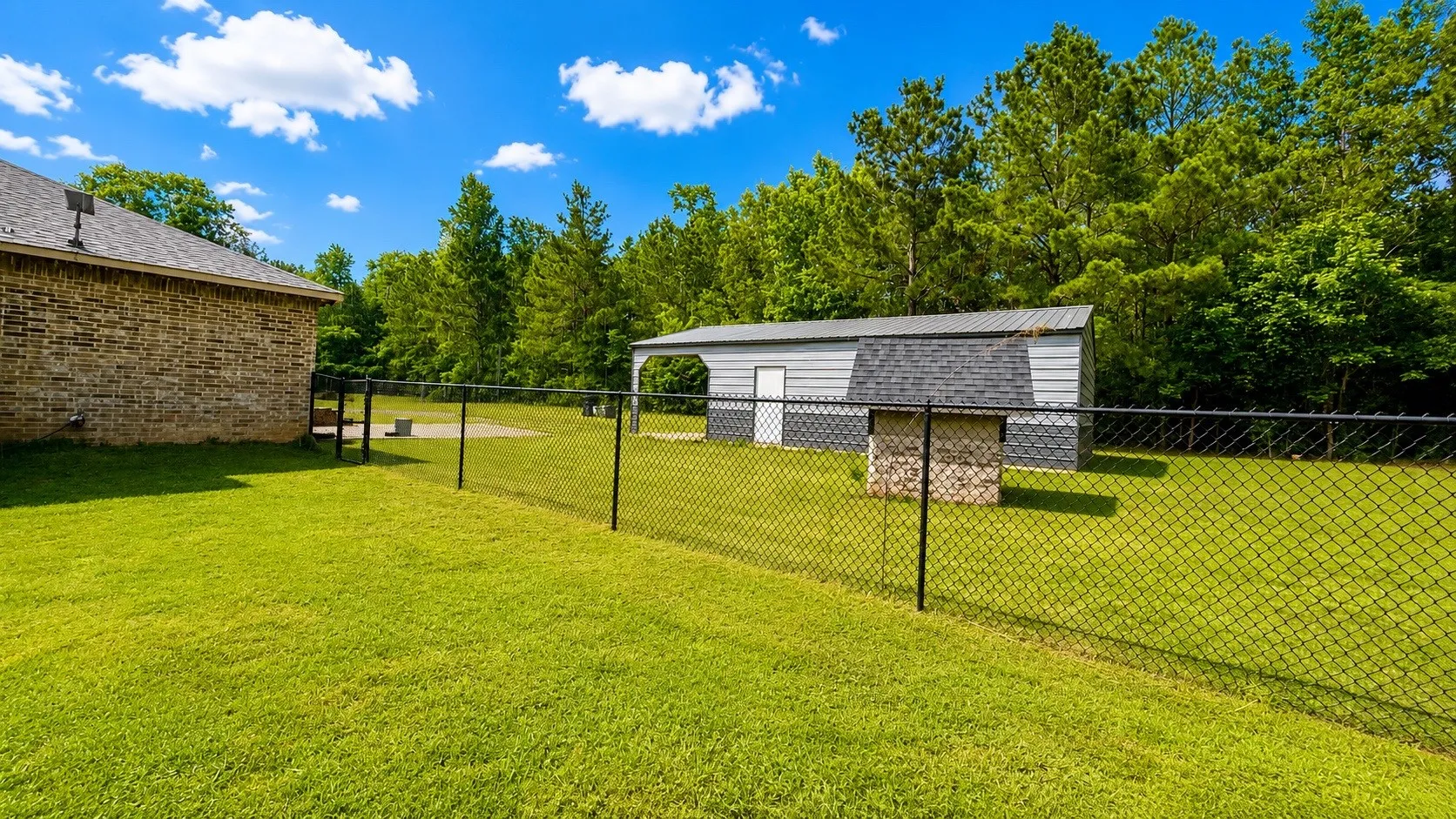 Expansive fenced backyard featuring a brick exterior, a detached storage building with an attached carport, and a built-in outdoor cooking station