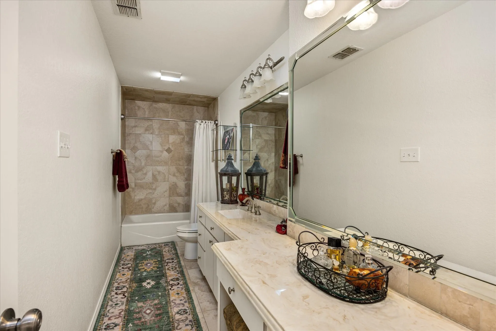 Bathroom featuring a large vanity with an integrated sink, an extensive mirror, and a full bathtub with tiled surround