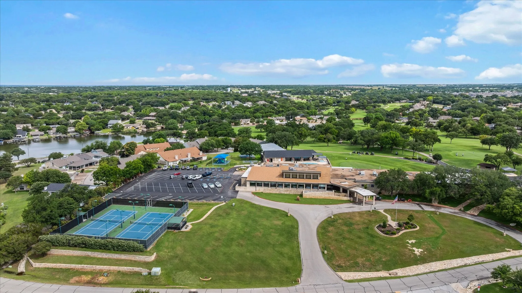 Expansive property featuring a central clubhouse, two tennis courts, an adjacent parking area, a manicured golf course