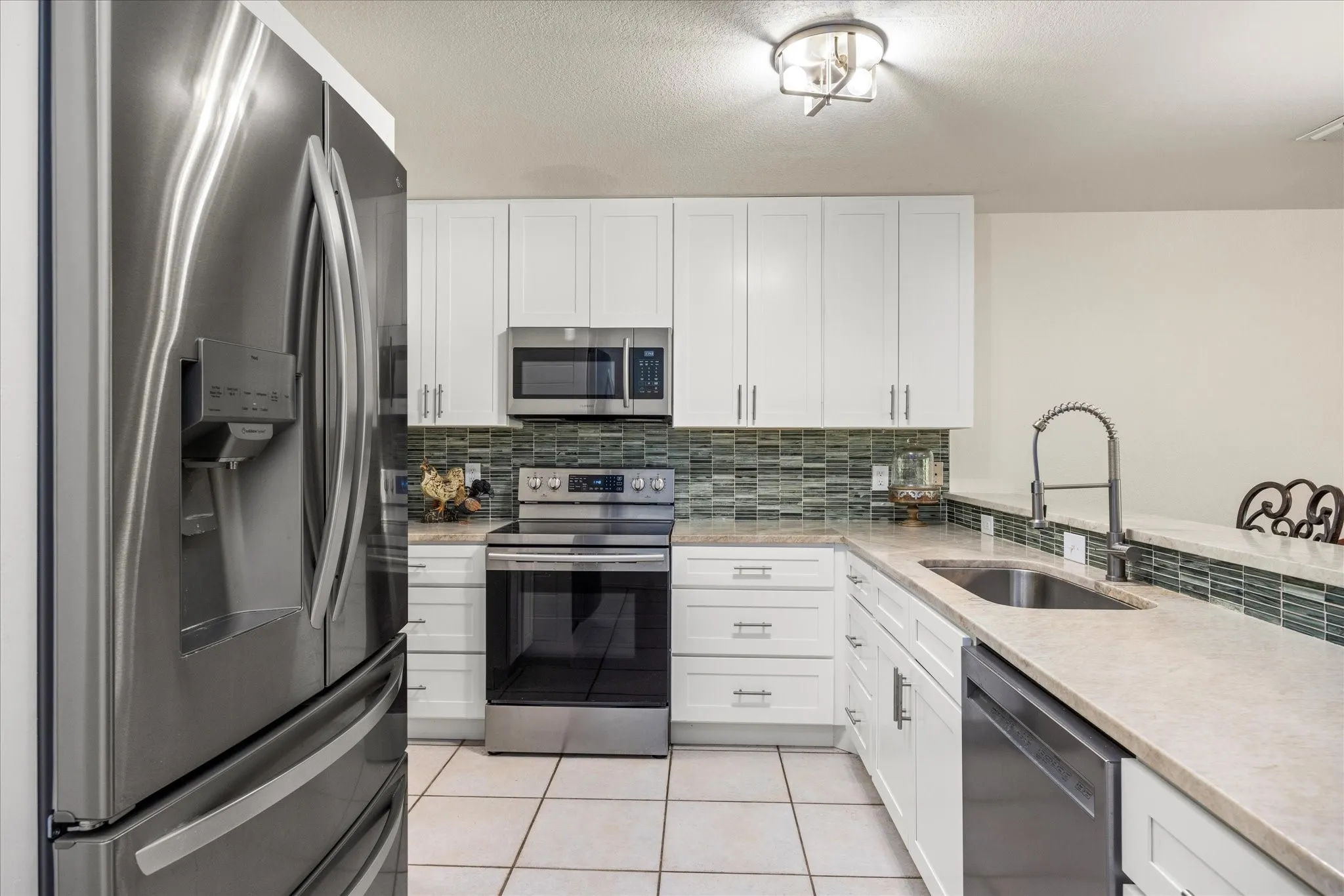 Modern kitchen featuring stainless steel appliances, white cabinetry, light-toned countertops, and tile flooring