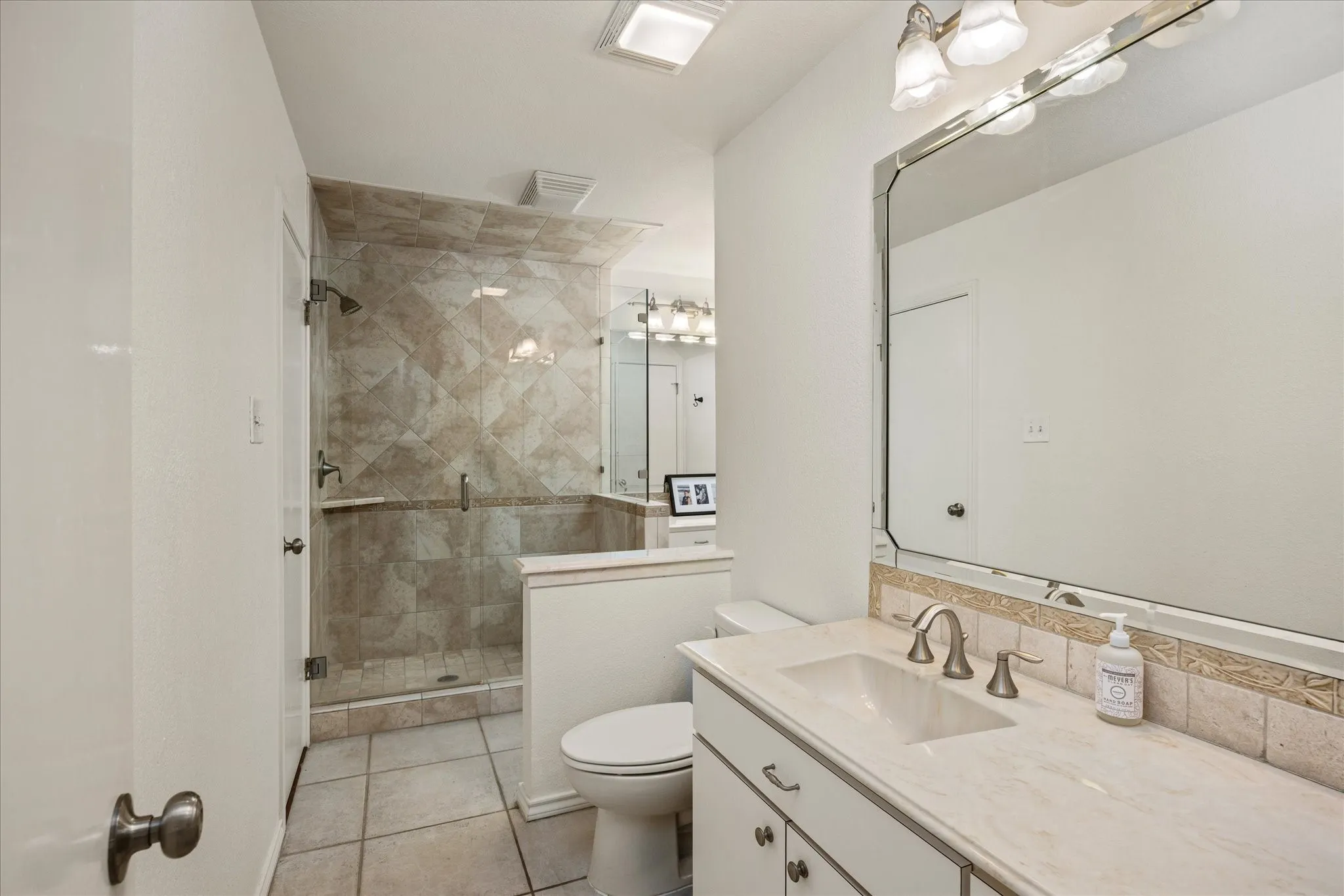 Bathroom featuring a glass-enclosed shower with tile surround, a vanity with an integrated sink, a large wall-mounted mirror, and tile flooring