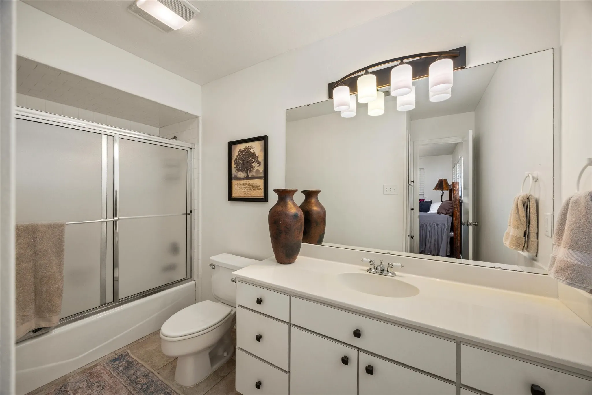 Bathroom featuring a single vanity with an integrated sink, a large wall-mounted mirror, and a combination tub/shower with frosted glass doors