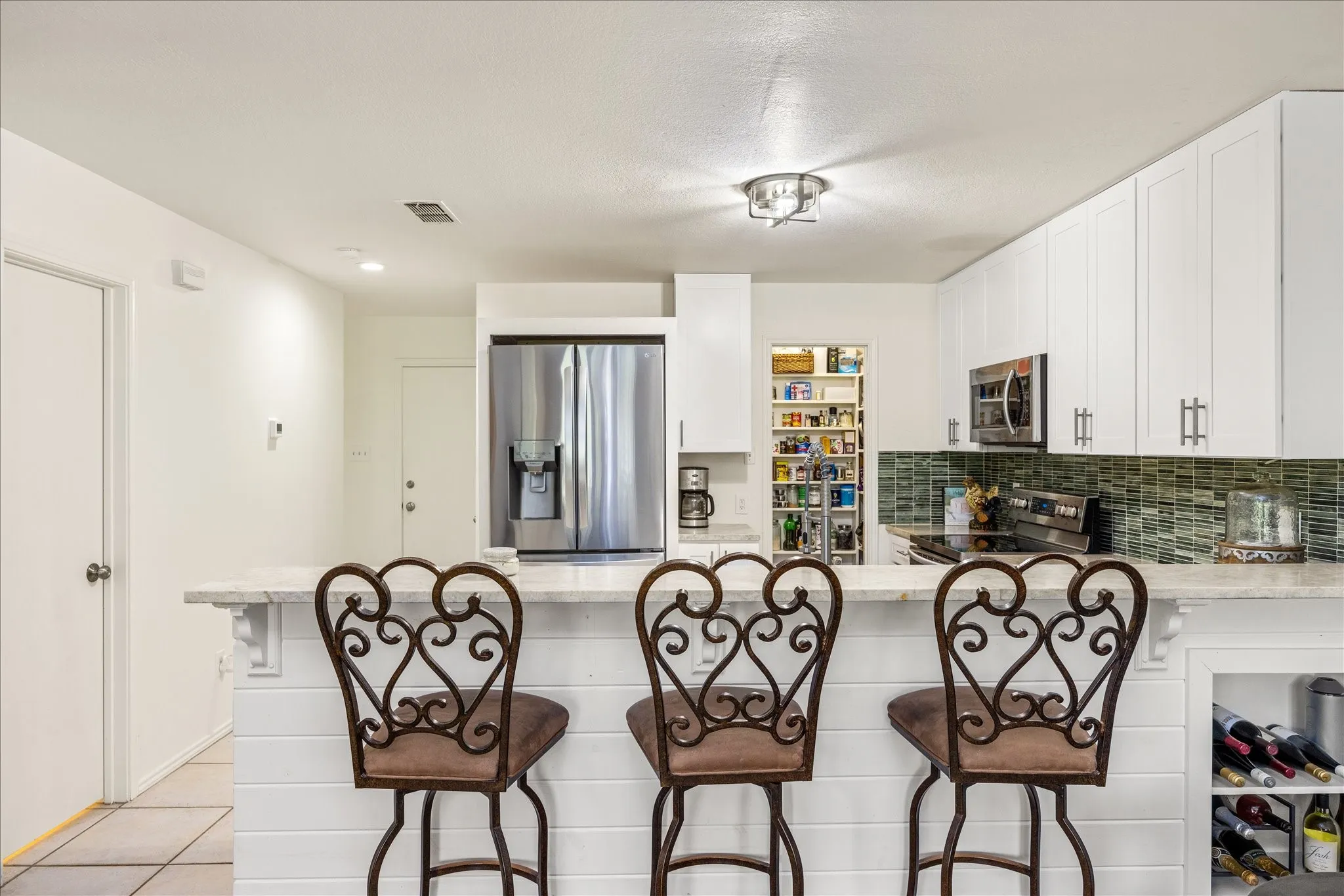 Kitchen featuring white shaker-style cabinetry, stainless steel appliances, a bar-height counter with shiplap-style paneling, a tiled backsplash, and a pantry with shelving
