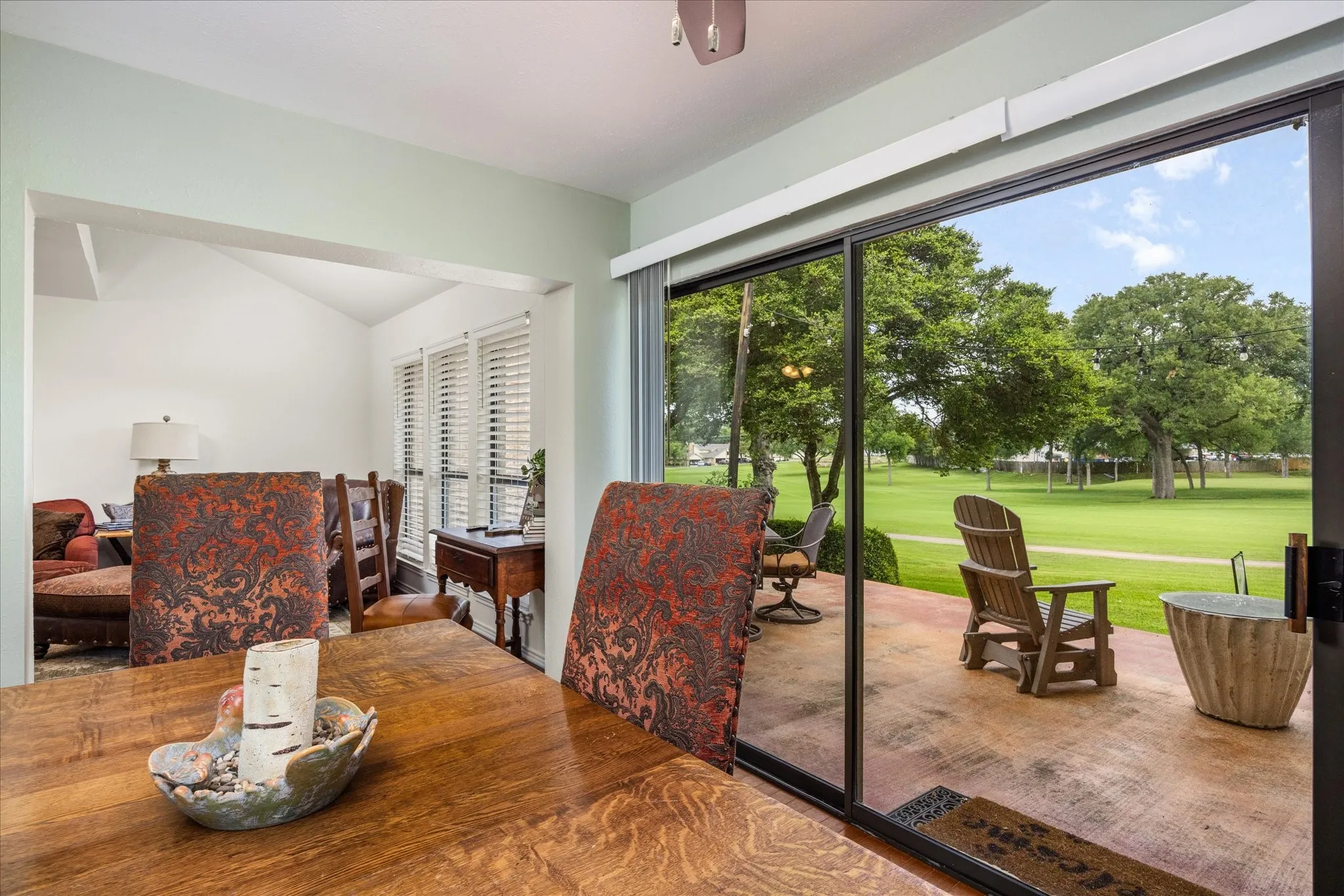 Patio access with sliding glass doors opening to a concrete patio and expansive green space with mature trees