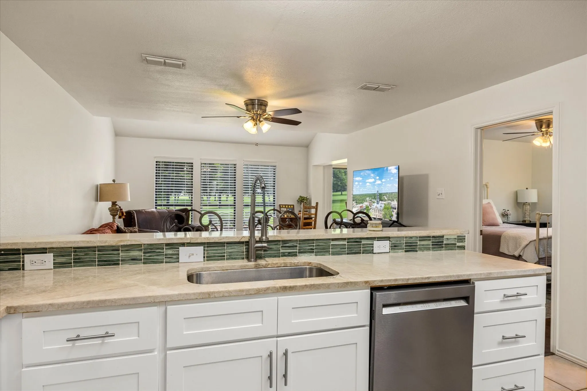 Kitchen featuring a stainless steel sink, white cabinetry with silver hardware, light-toned countertop, and a green tile backsplash