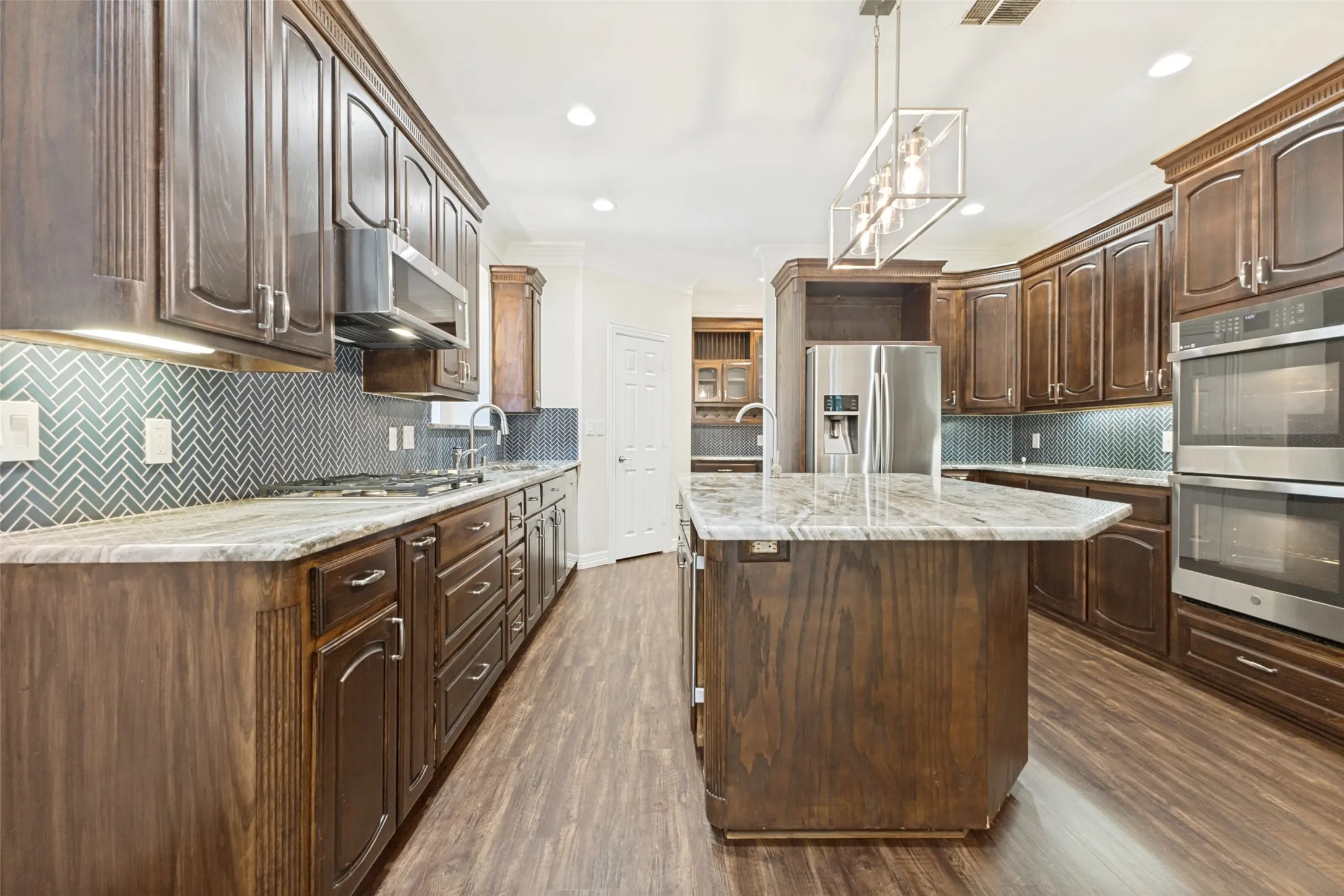 Gourmet kitchen featuring warm wood cabinetry, gorgeous countertops, herringbone tile backsplash, stainless steel appliances, and a central island with bar seating.