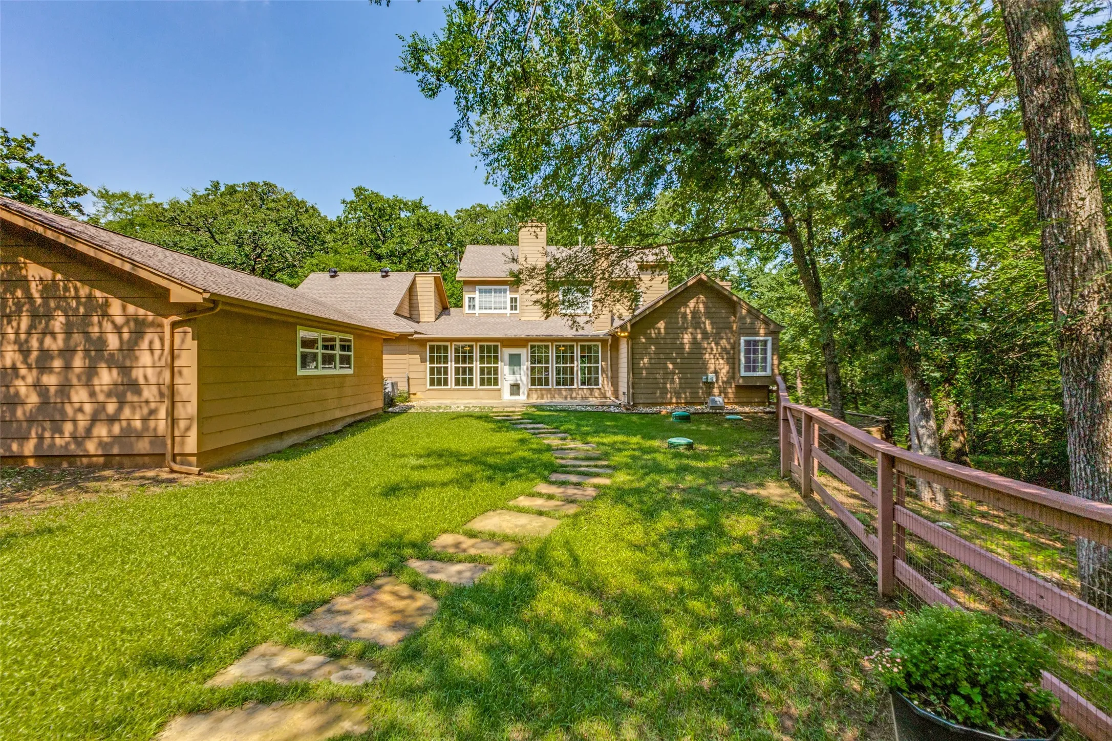 Expansive backyard featuring a stone pathway, mature trees, a wood fence.
