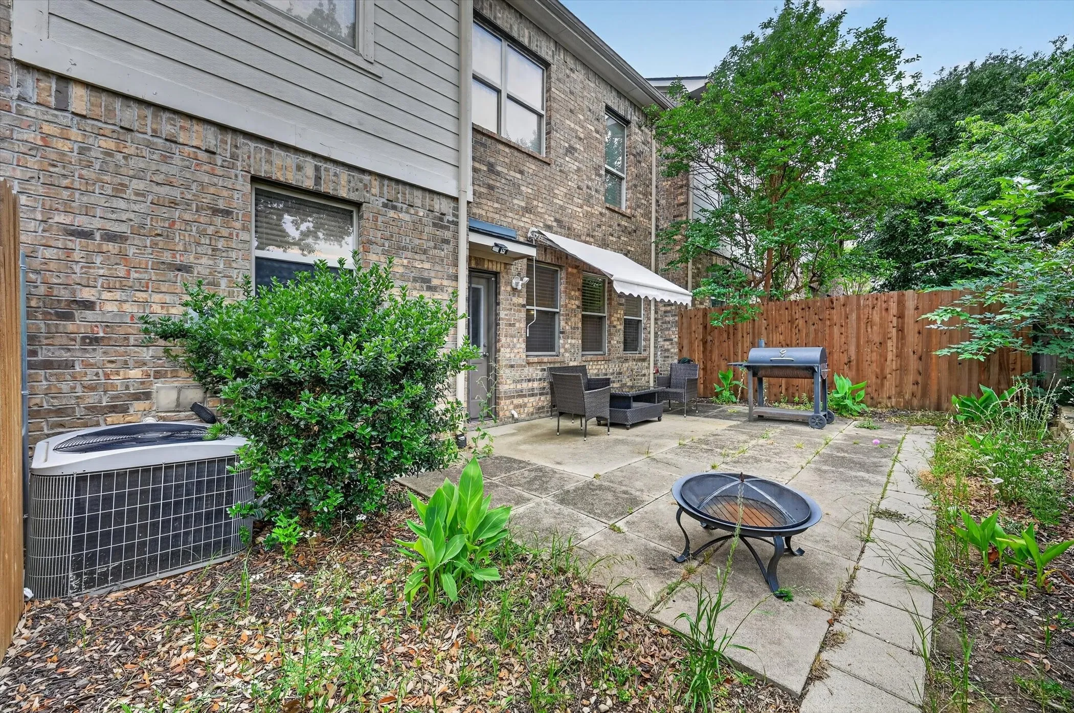 Expansive rear patio featuring large format pavers, a partial privacy fence, and mature perimeter trees
