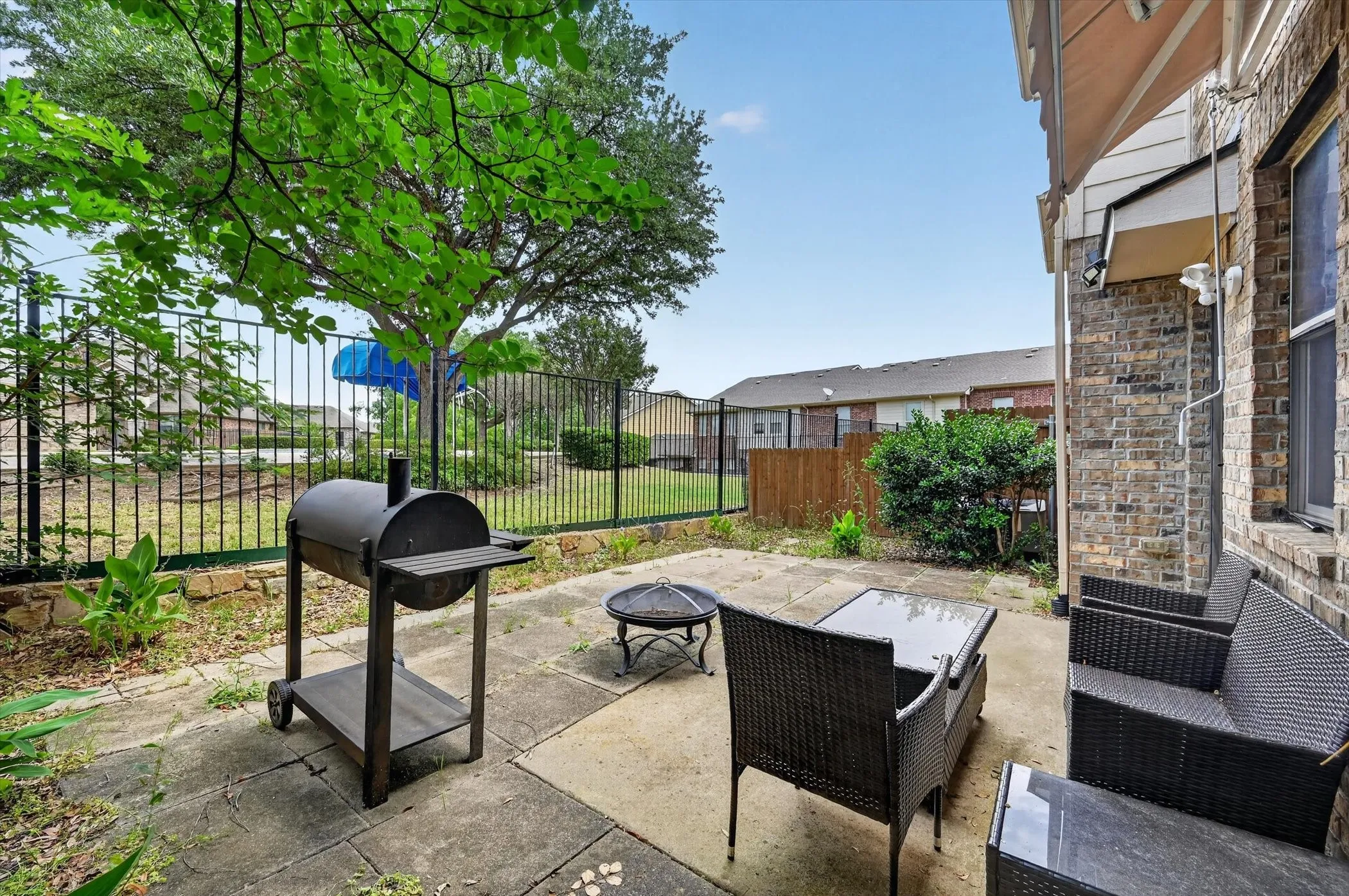 Outdoor patio featuring concrete pavers, a partial brick exterior, and a black wrought iron fence