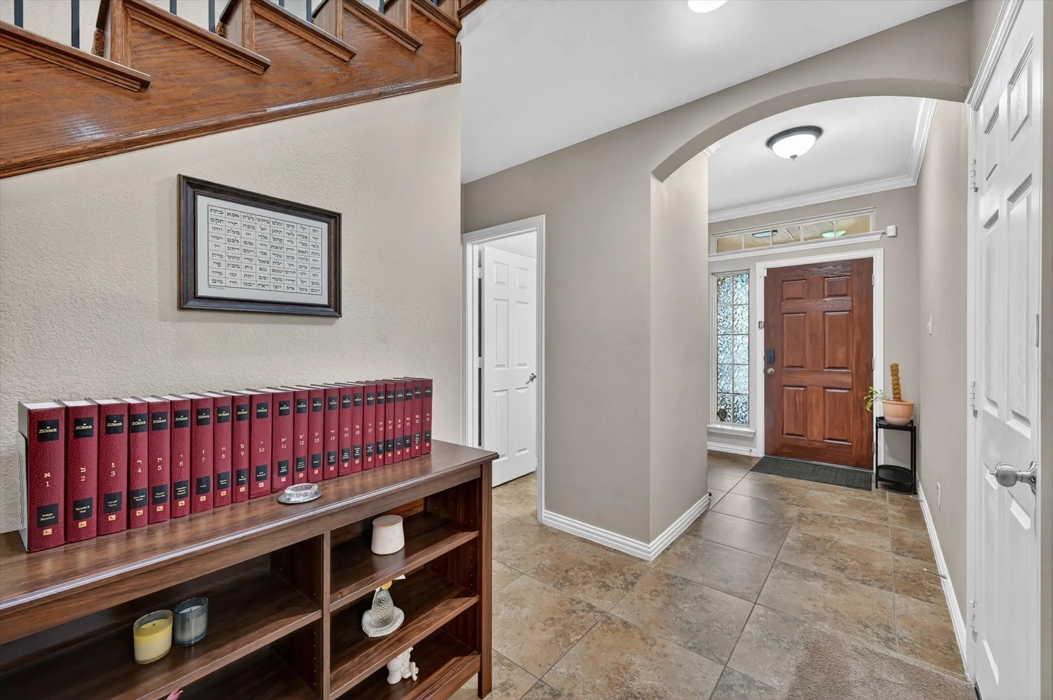Foyer featuring durable tile flooring, a solid wood entry door with decorative glass sidelight and transom, a wide archway, and a staircase with wood treads and banister