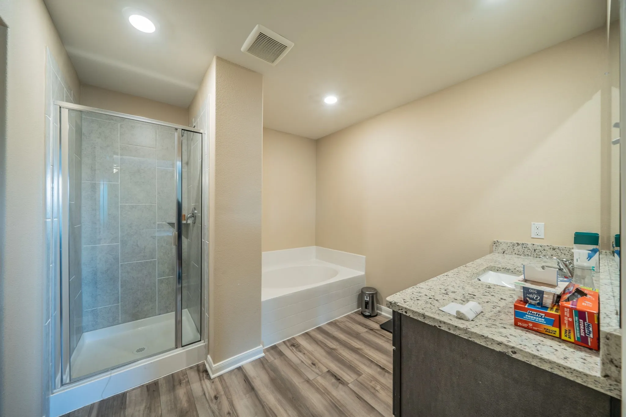Full bathroom featuring a walk-in shower with glass enclosure, a built-in soaking tub, wood-finish flooring, and a vanity with a stone-finish countertop