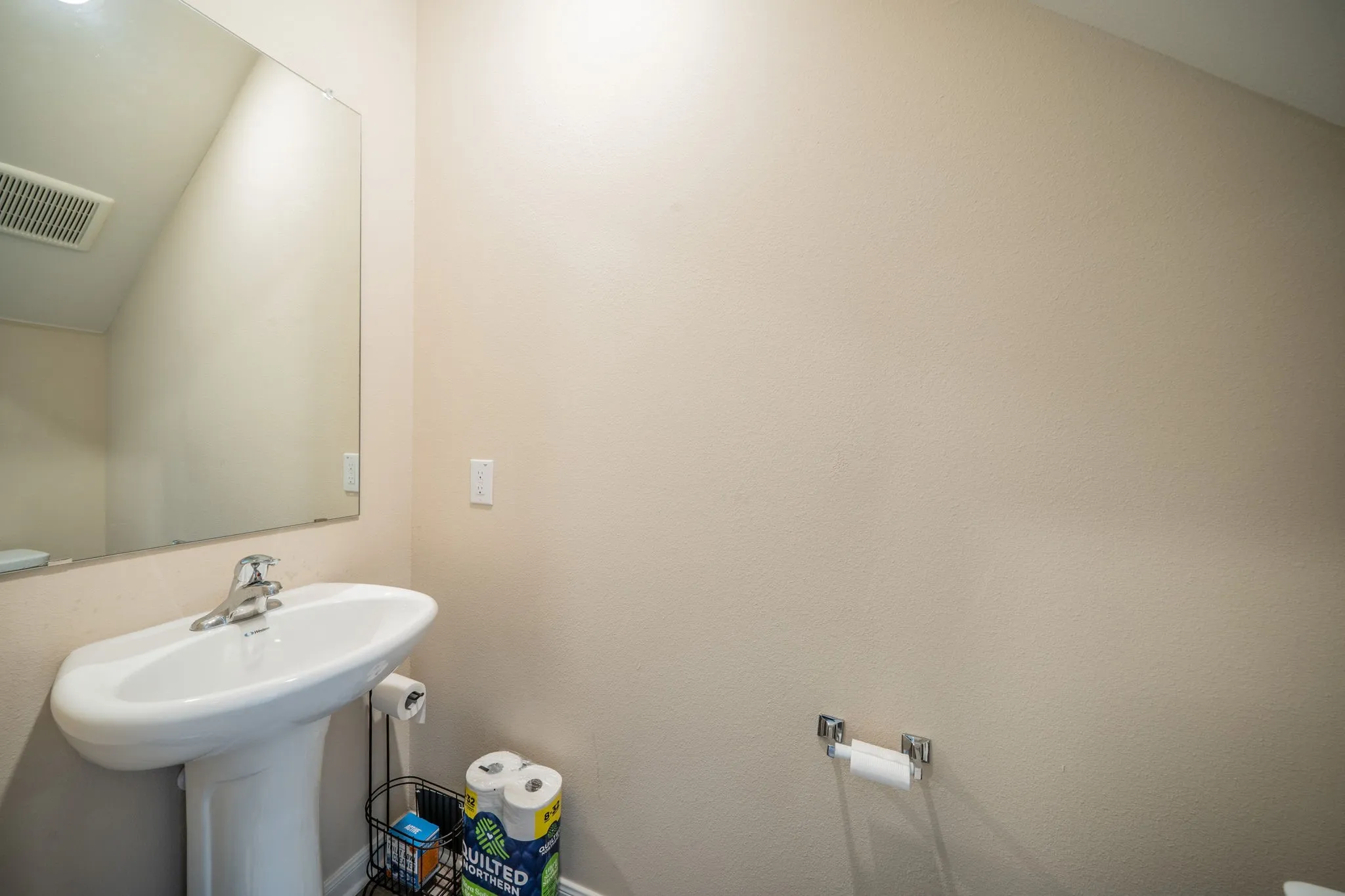 Pedestal sink with chrome faucet, large wall-mounted mirror, and neutral wall paint
