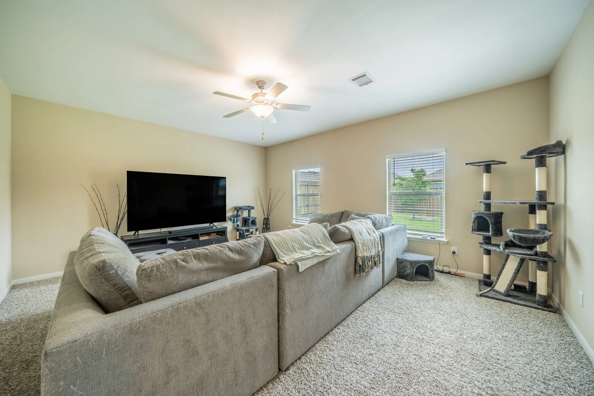 Carpeted living area featuring a ceiling fan with integrated lighting, multiple windows, and a neutral color palette