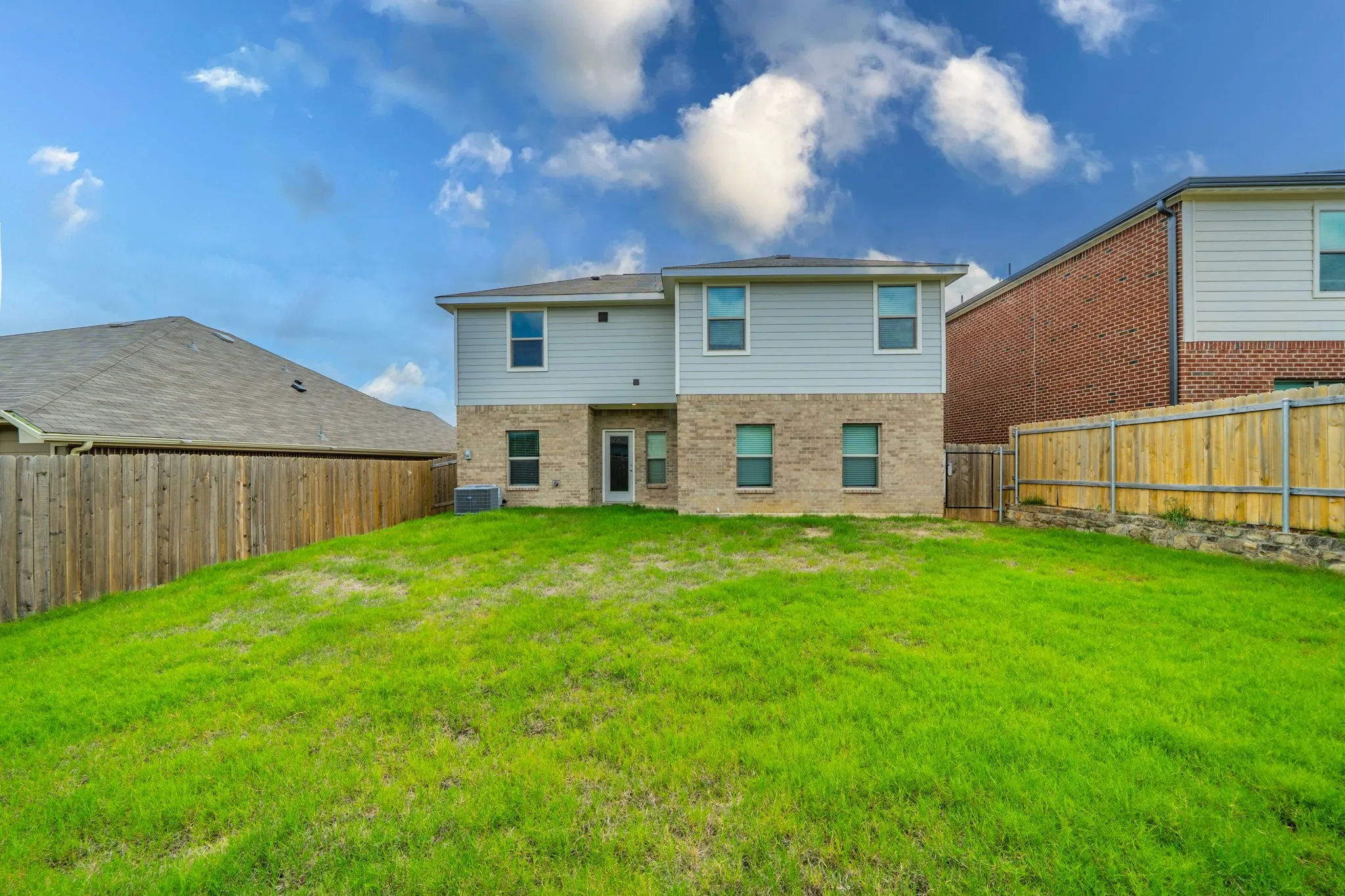 Rear exterior featuring a two-story design with brick and siding, a ground-level door, multiple windows, and a private fenced yard