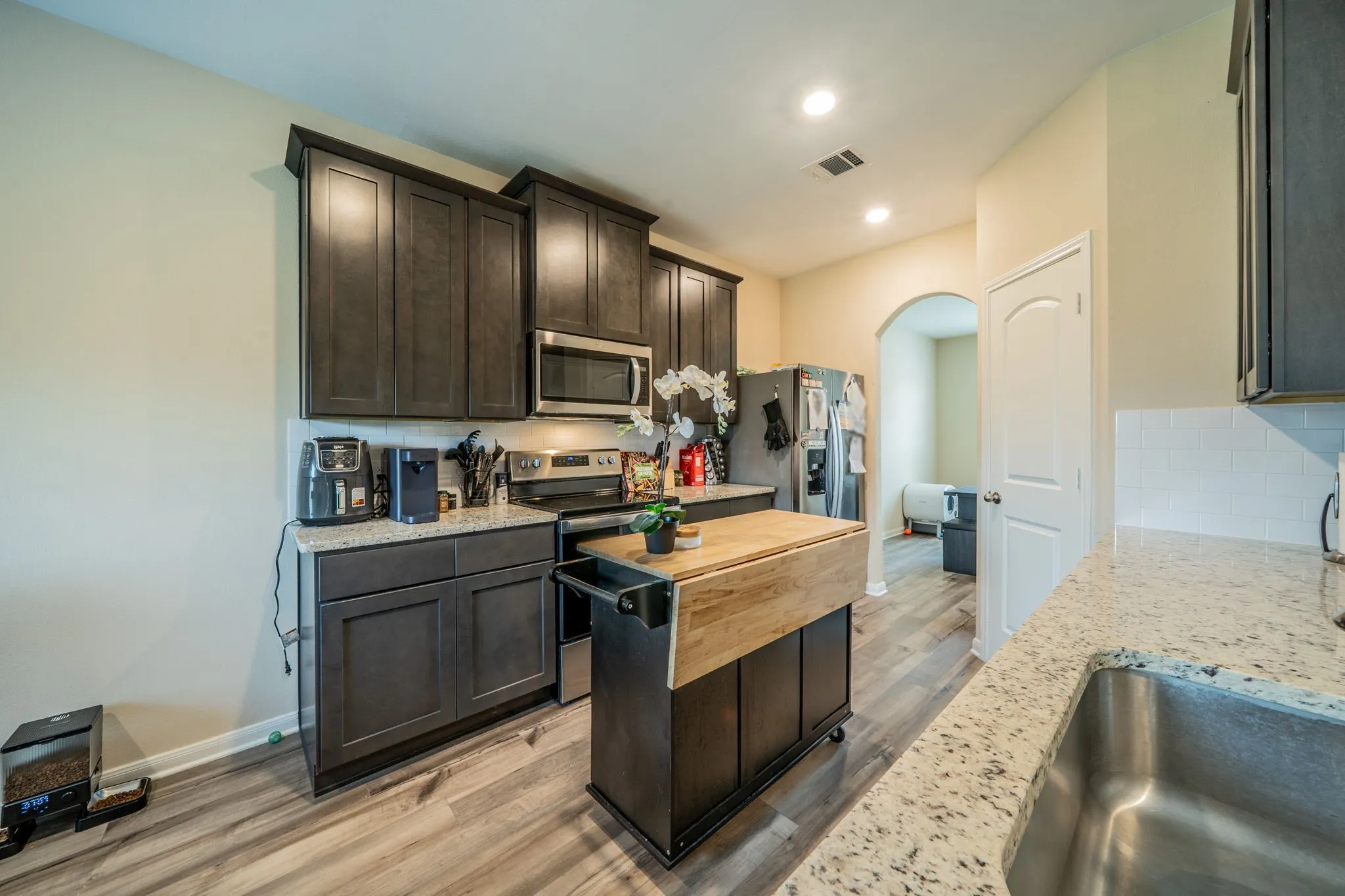 Spacious kitchen with dark wood-finish cabinetry, stainless steel appliances, granite-style countertops, and light wood-finish flooring