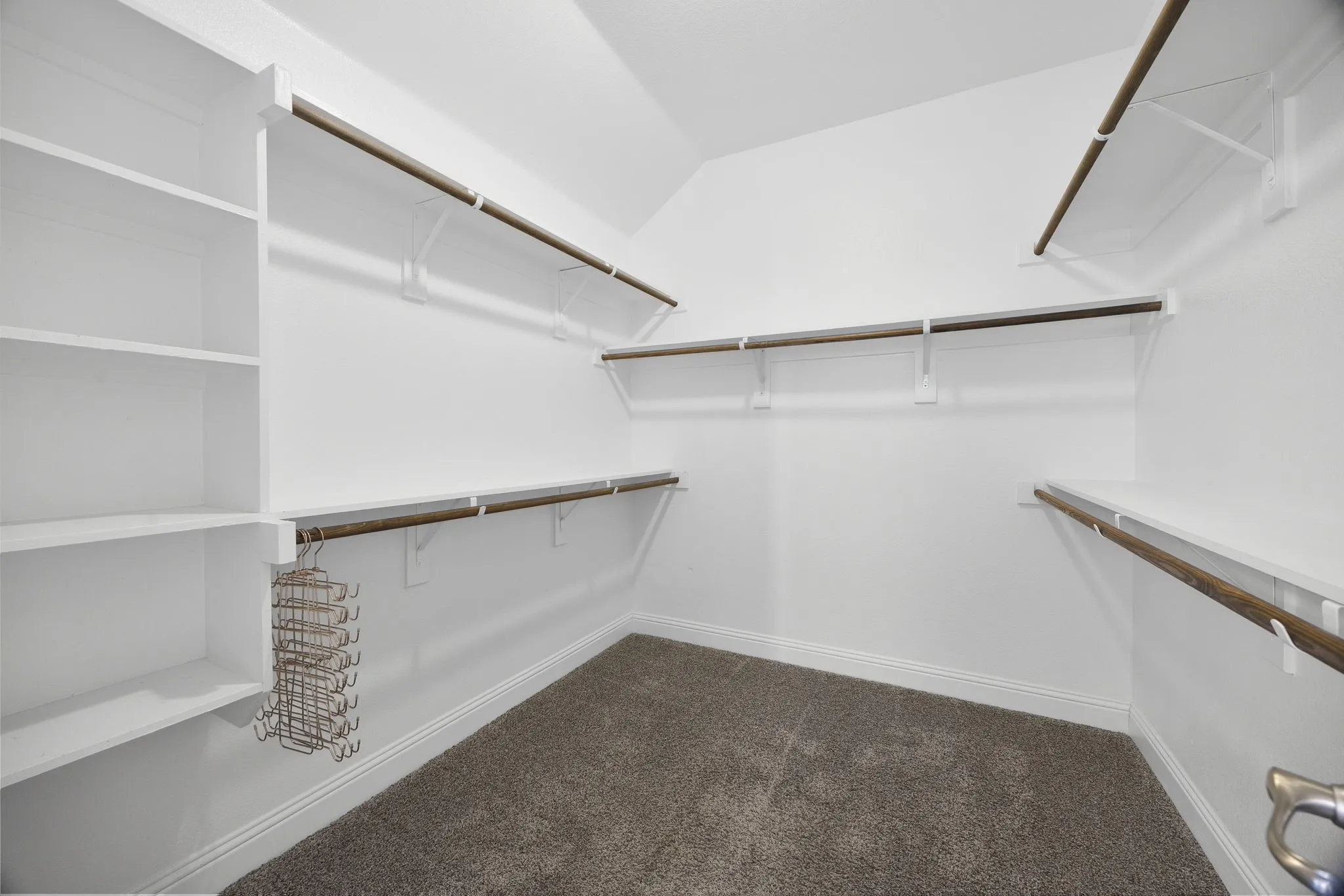 Walk in primary closet with shelving and hanging rods.