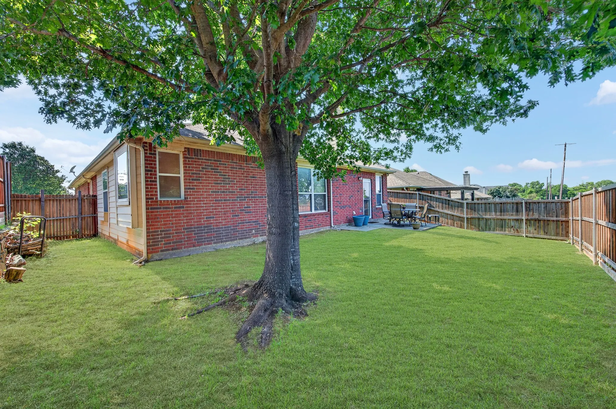 Expansive backyard featuring a mature shade tree, a brick exterior, a wood fence, a bay window, and a patio area