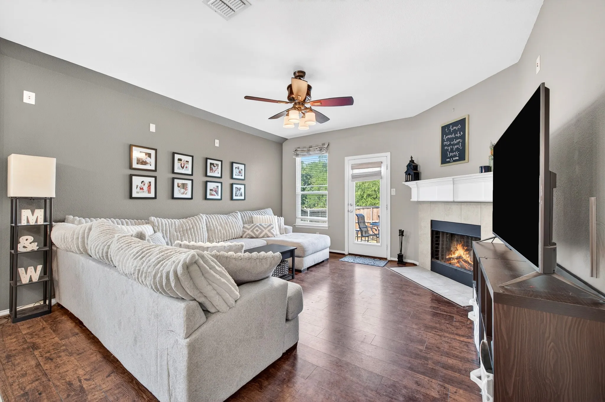 Living area featuring wood-finish flooring, a ceiling fan, and a fireplace with a white mantel and tile surround