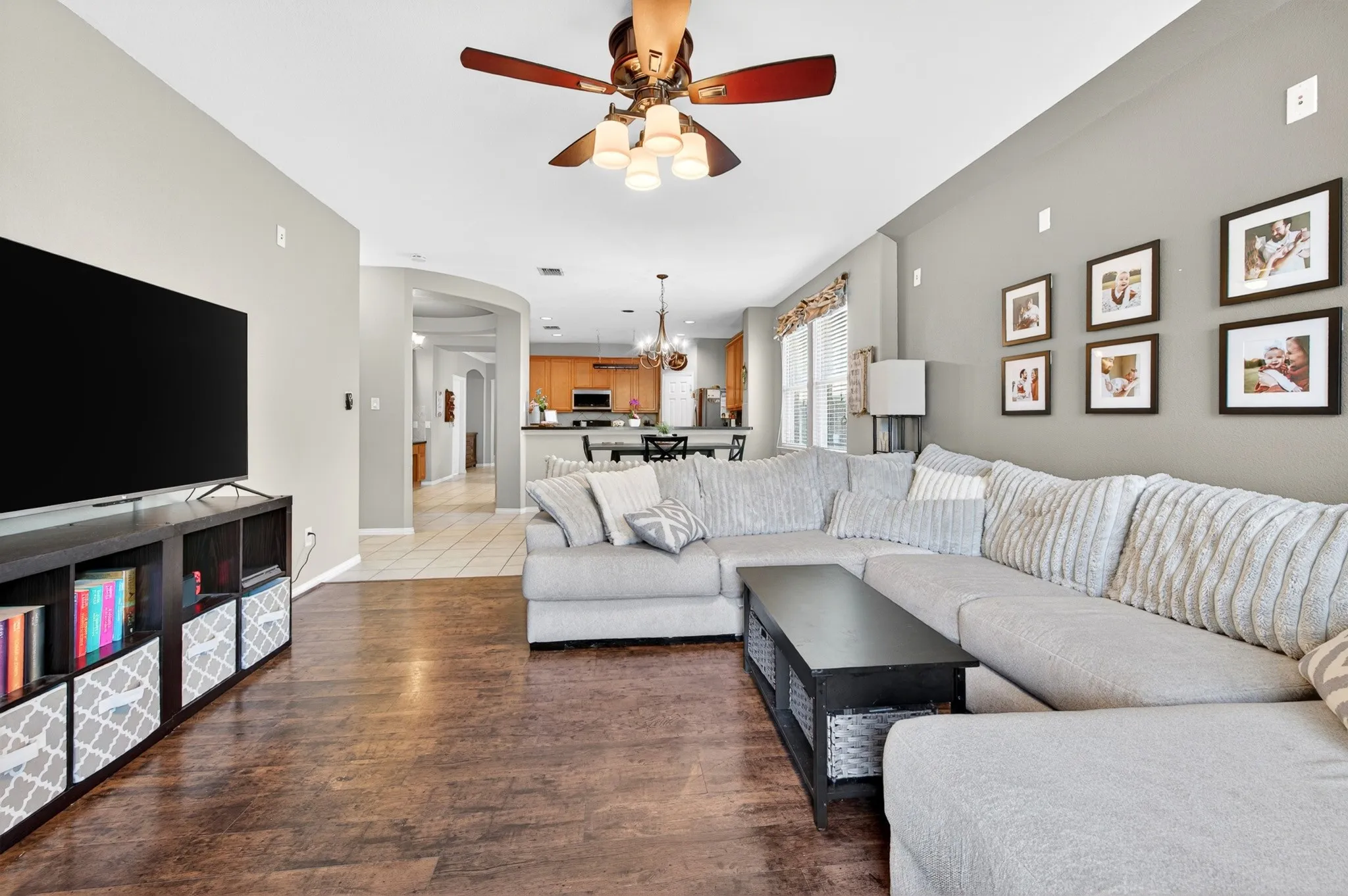 Spacious living area featuring wood-finish flooring, light gray walls, and a ceiling fan with integrated lighting
