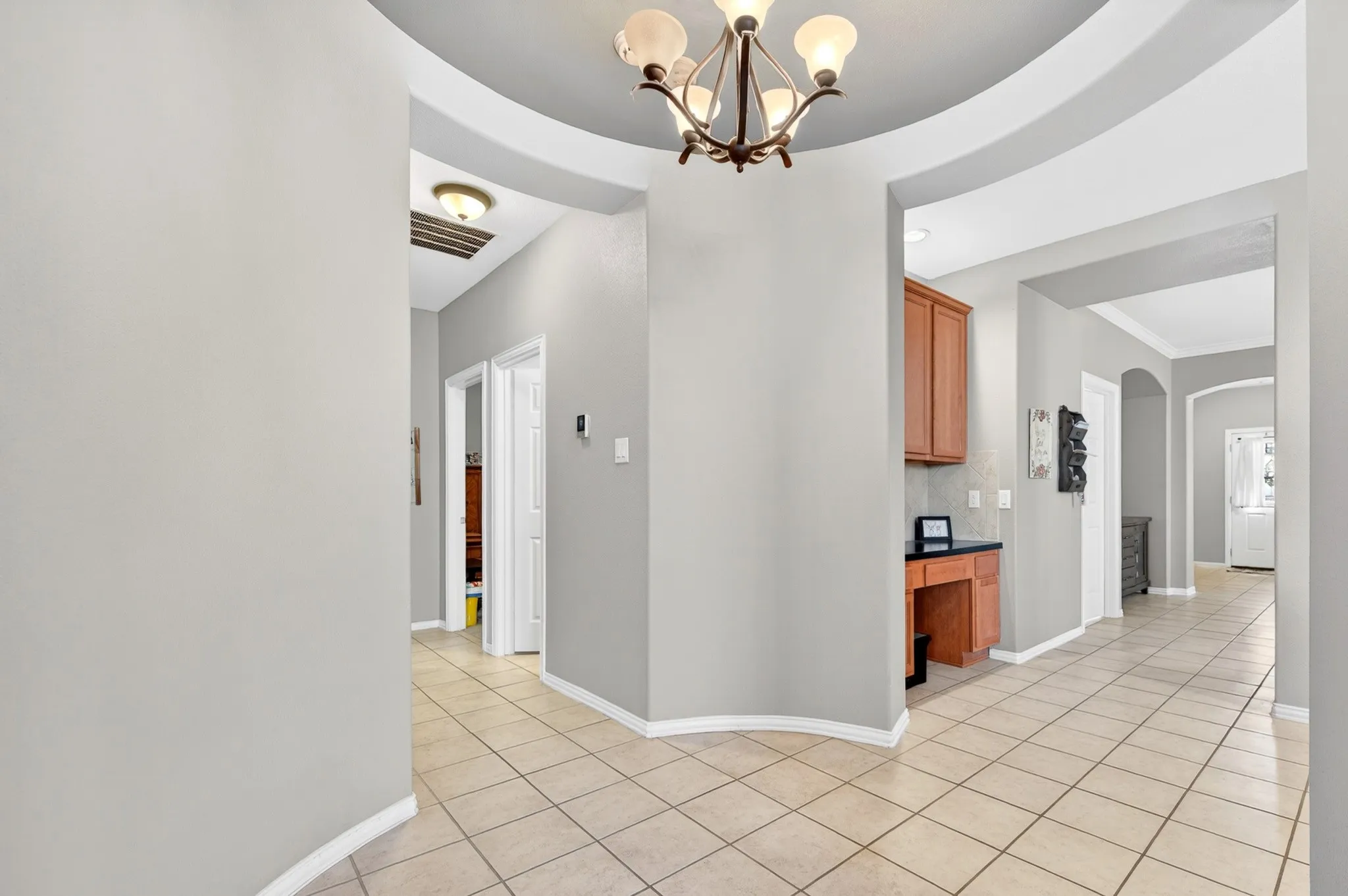 Hallway featuring a built-in desk with overhead cabinetry, tiled flooring, arched doorways, and a ceiling-mounted light fixture