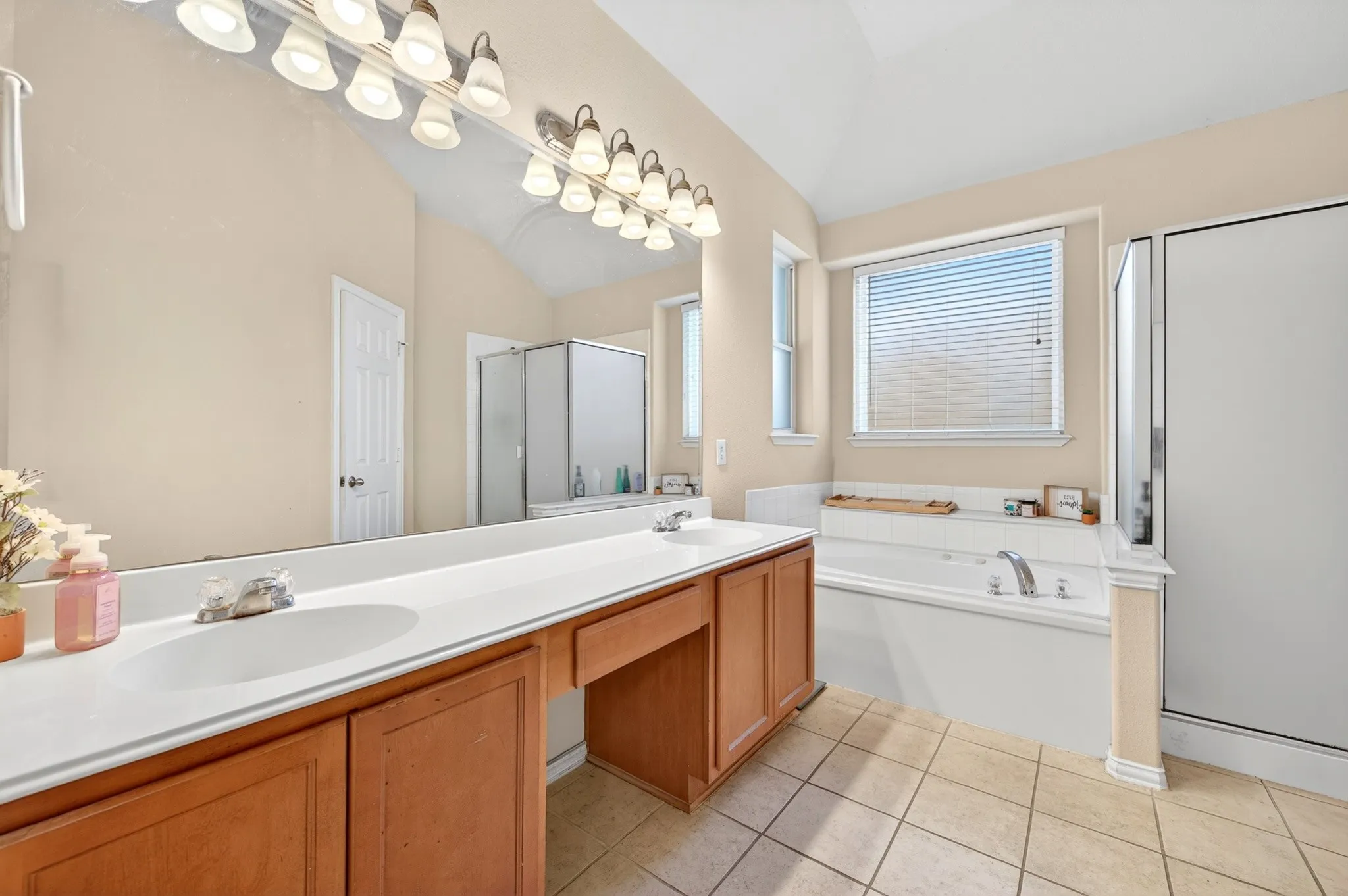 Bathroom featuring a double vanity with wood cabinetry, a built-in garden tub, a separate shower with a glass enclosure, a window with blinds, and tiled flooring
