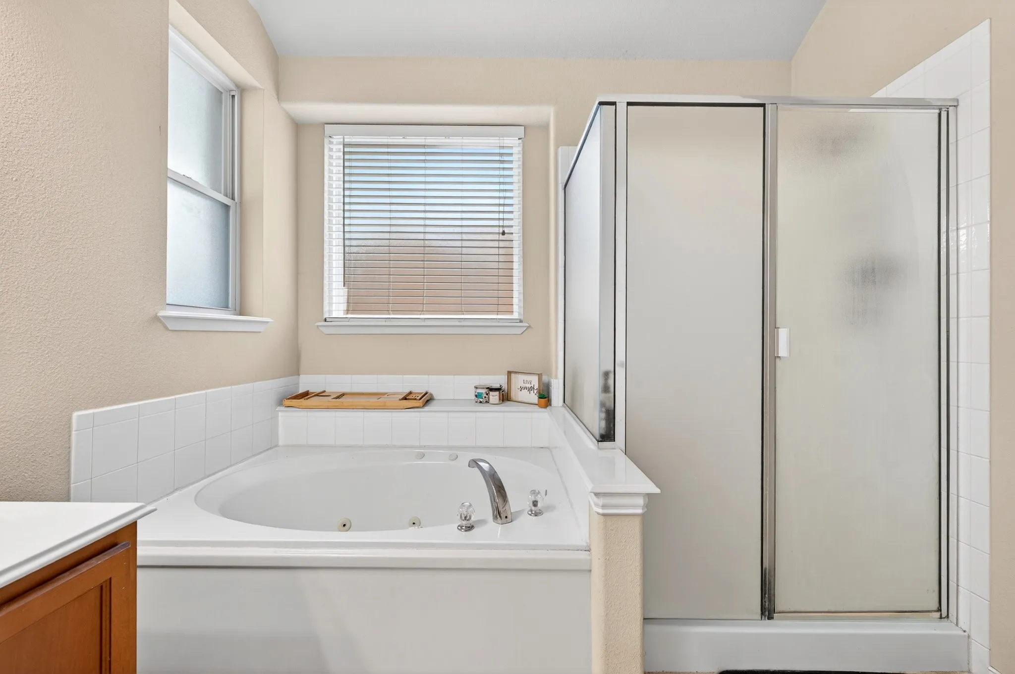 Bathroom featuring a built-in jetted tub, a separate shower with frosted glass doors, and two windows with blinds providing natural light