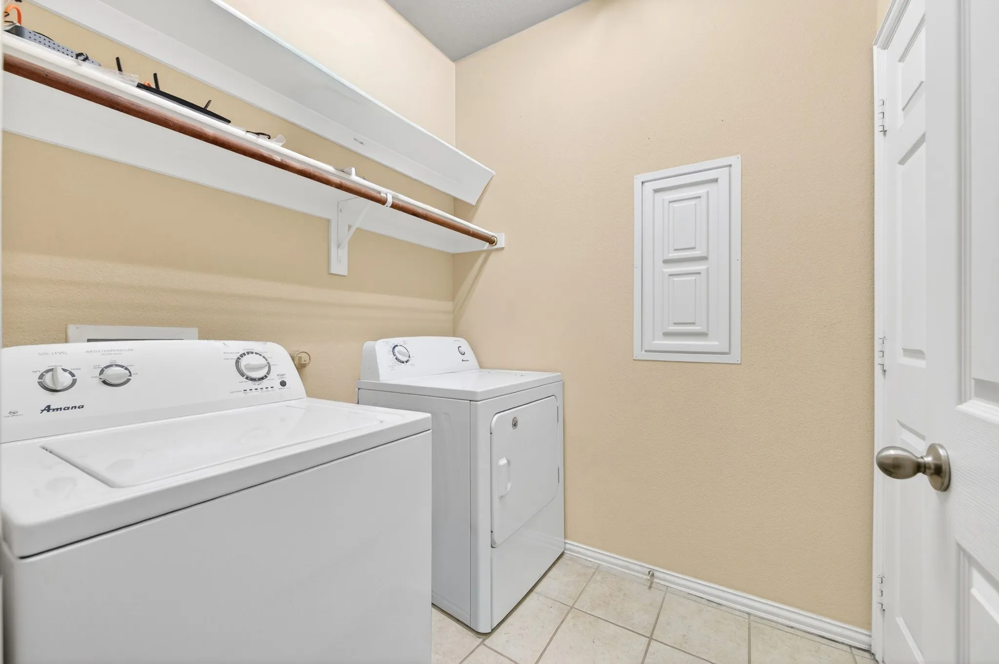 Dedicated utility room featuring tile flooring, neutral wall tones, and built-in shelving with a clothes rod